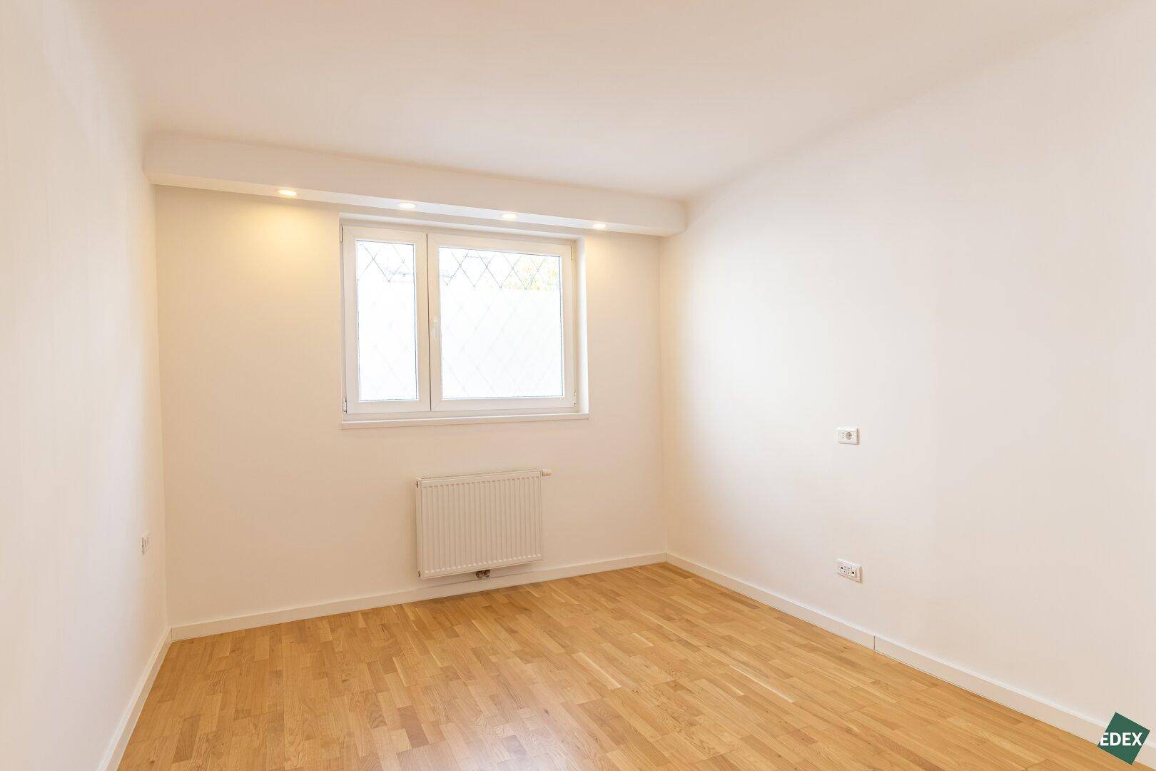 Helles Schlafzimmer mit Parkettboden und großem Fenster, ideal für natürliche Belichtung.