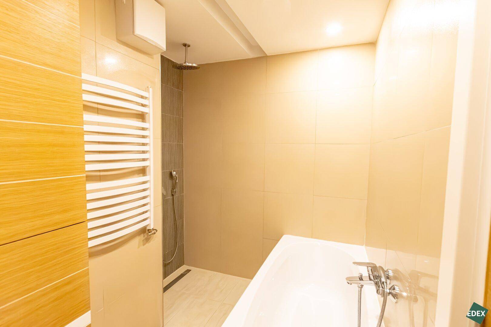 Elegantes Badezimmer mit Badewanne, begehbarer Dusche und beigefarbenen Fliesen.