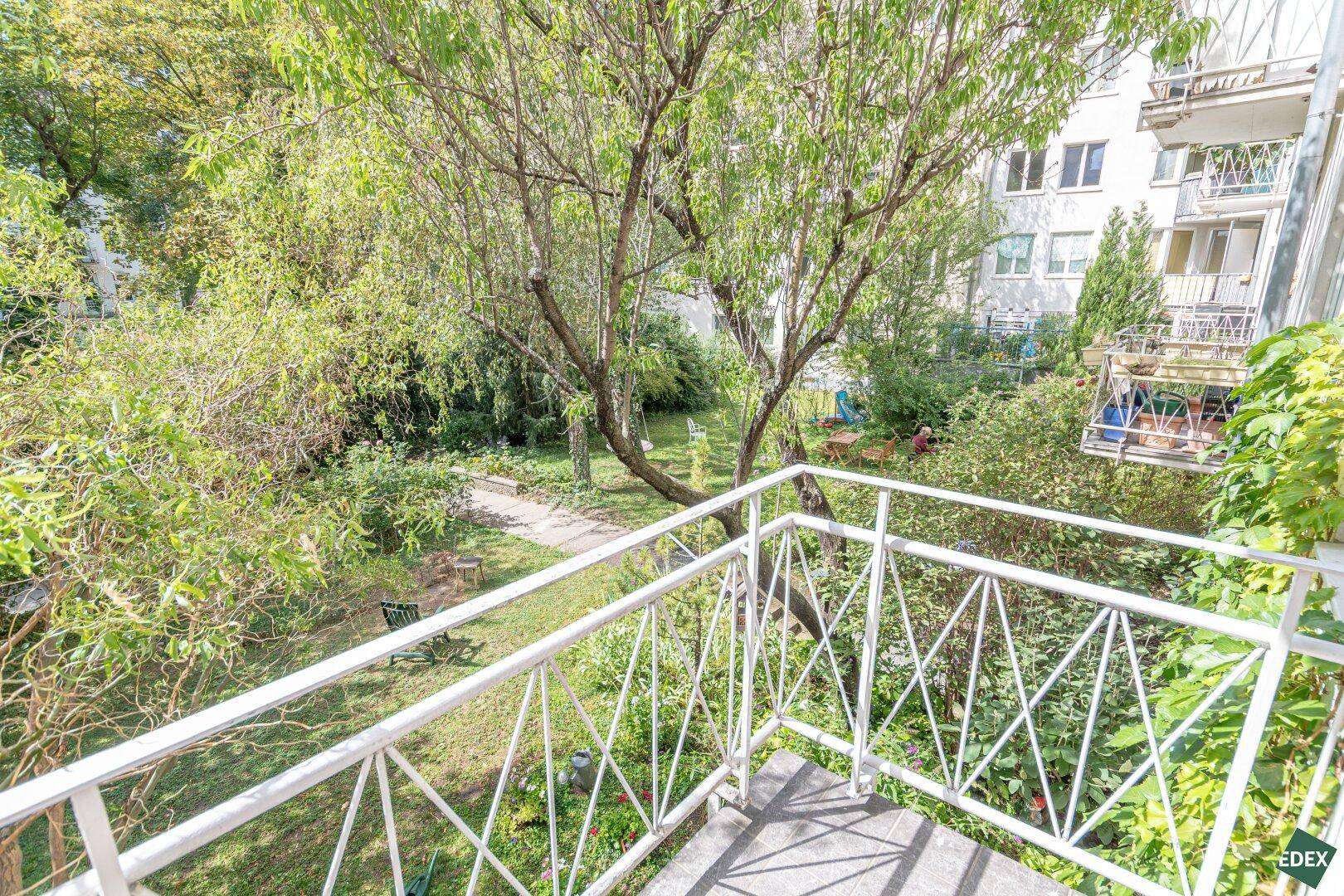 Kleiner Balkon mit Blick auf den grünen Innenhof und alte Bäume.