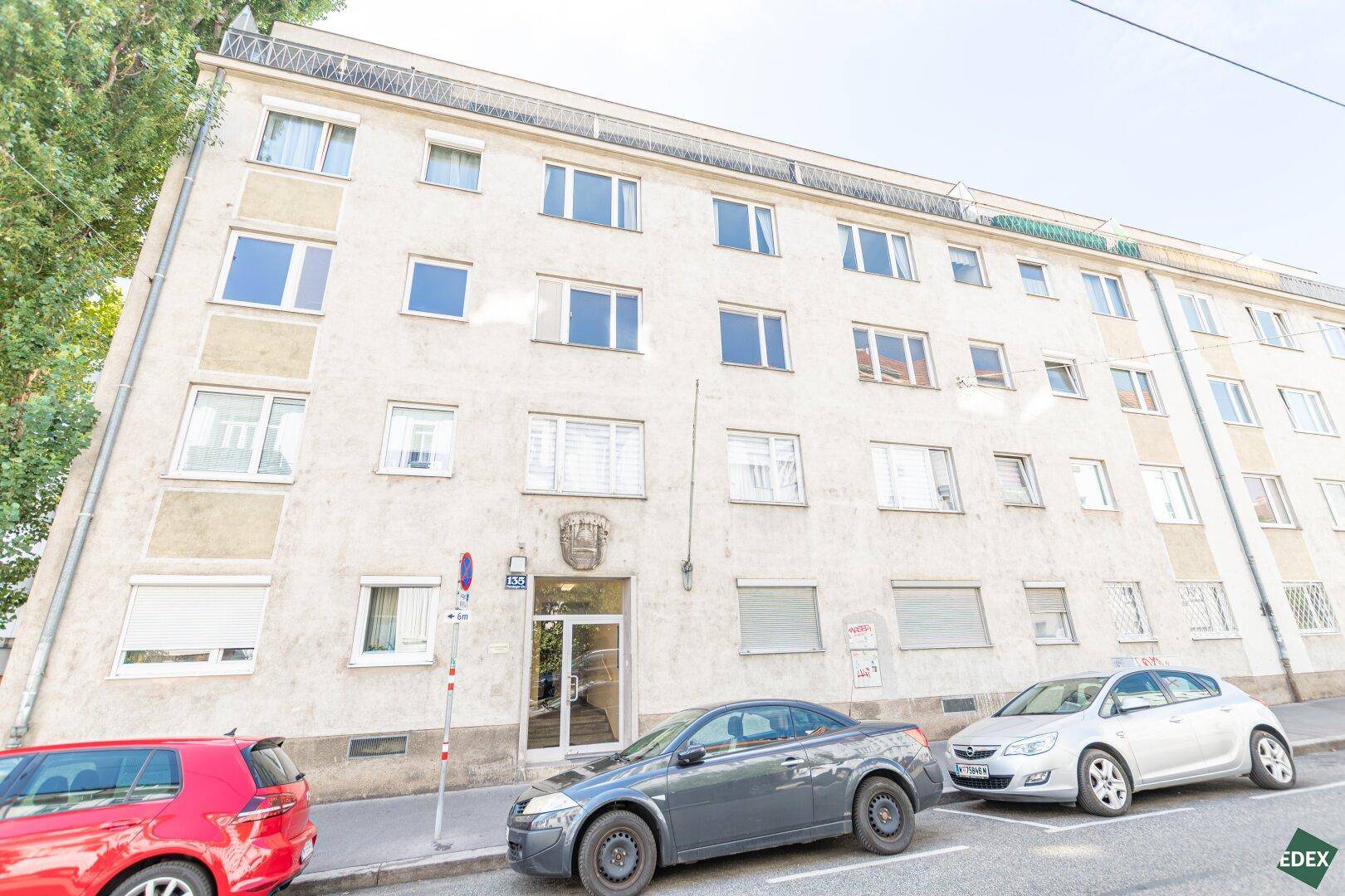 Mehrfamilienhaus mit klassischer Fassade und parkenden Autos davor.