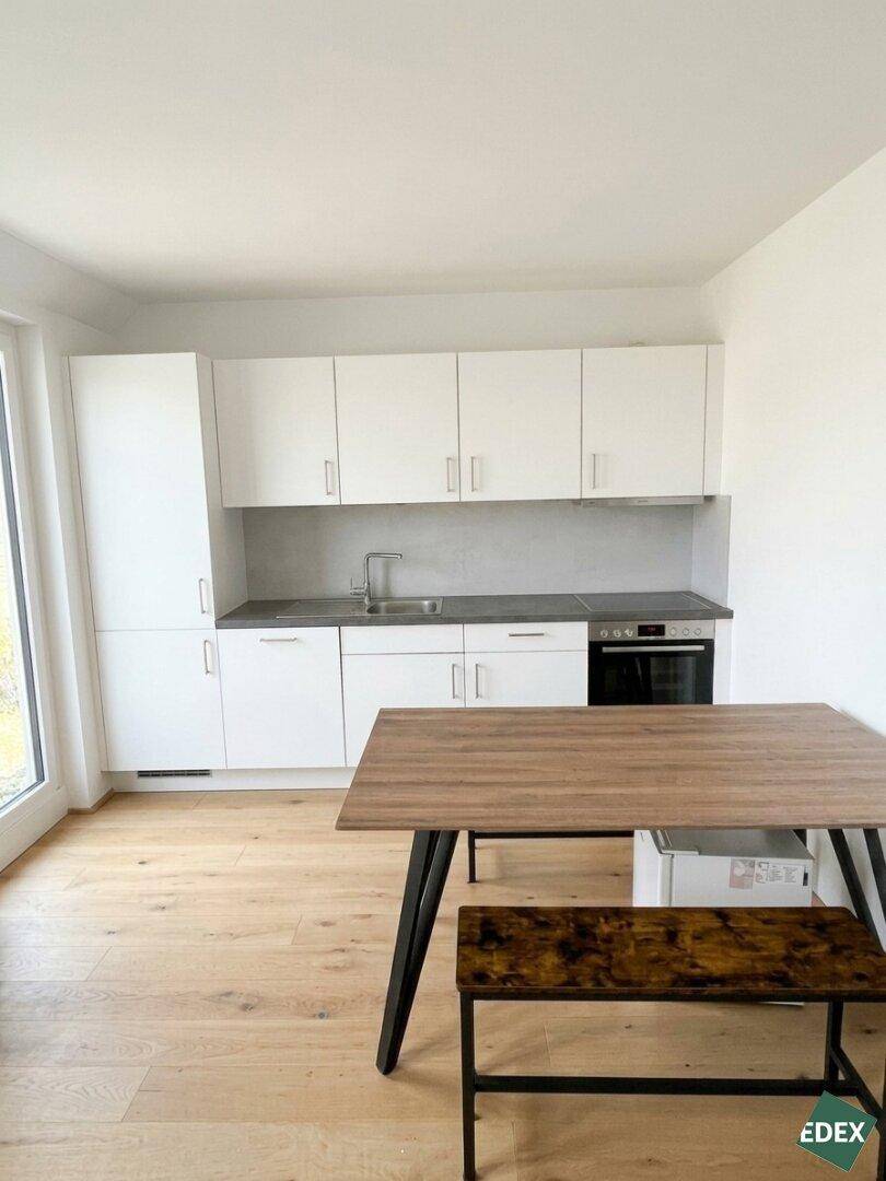 Moderne Einbauküche mit weißen Schränken, dunkler Arbeitsplatte und Esstisch.