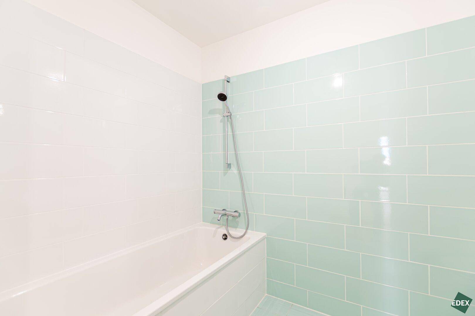 Modernes Badezimmer mit Badewanne und hellgrünen Fliesen an den Wänden, in neuwertigem Zustand.