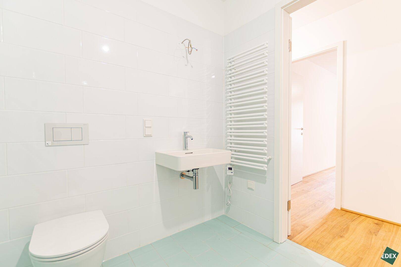 Helles Badezimmer mit wandhängendem WC, Waschbecken und beheiztem Handtuchhalter, modern gefliest.