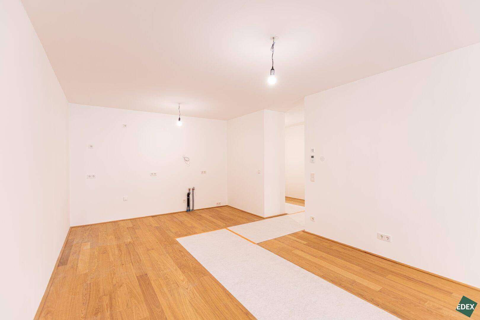 Leerer Raum mit Holzboden und Anschlüssen für eine moderne Einbauküche, bereit zur Installation.