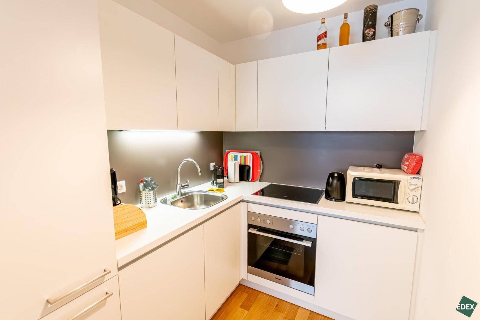 Moderne Einbauküche mit weißen Hochglanzfronten, Induktionskochfeld, Backofen und Mikrowelle.
