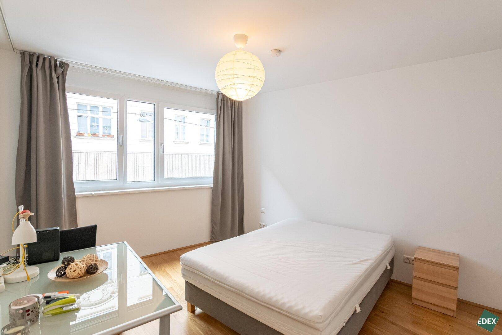 Helles Schlafzimmer mit Doppelbett, Schreibtisch und großen Fenstern für viel Tageslicht.