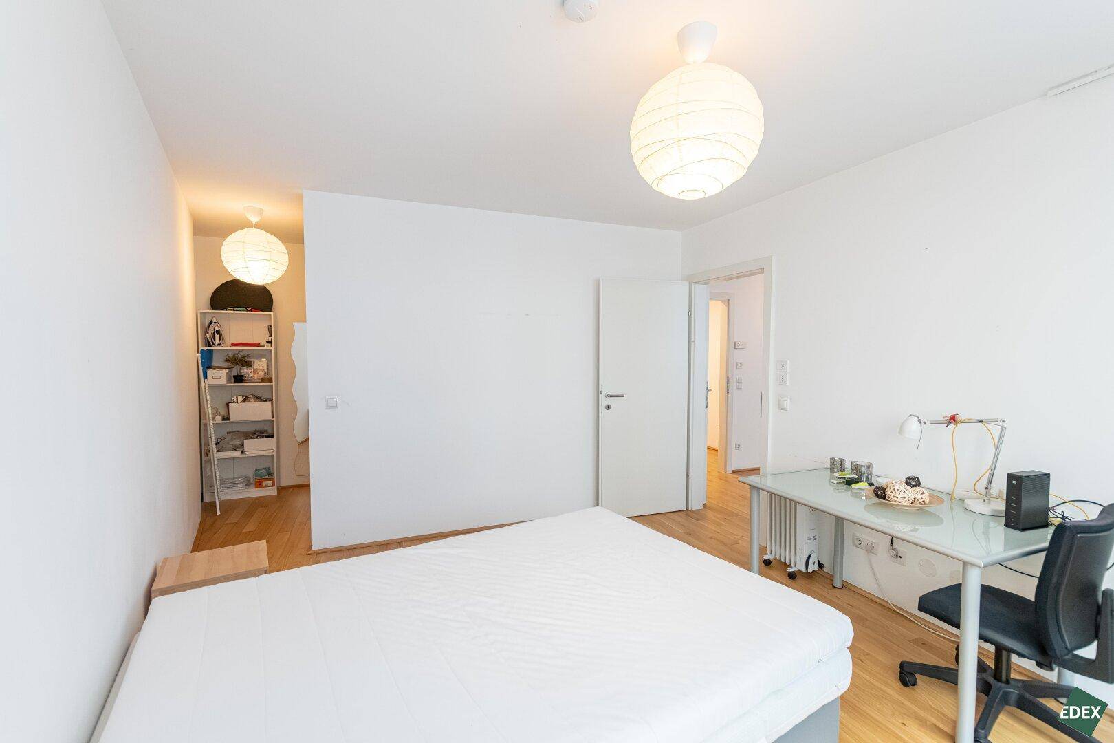 Schlafzimmer mit Bett, Schreibtisch und einem offenen Regalbereich für Kleidung und Ablage.