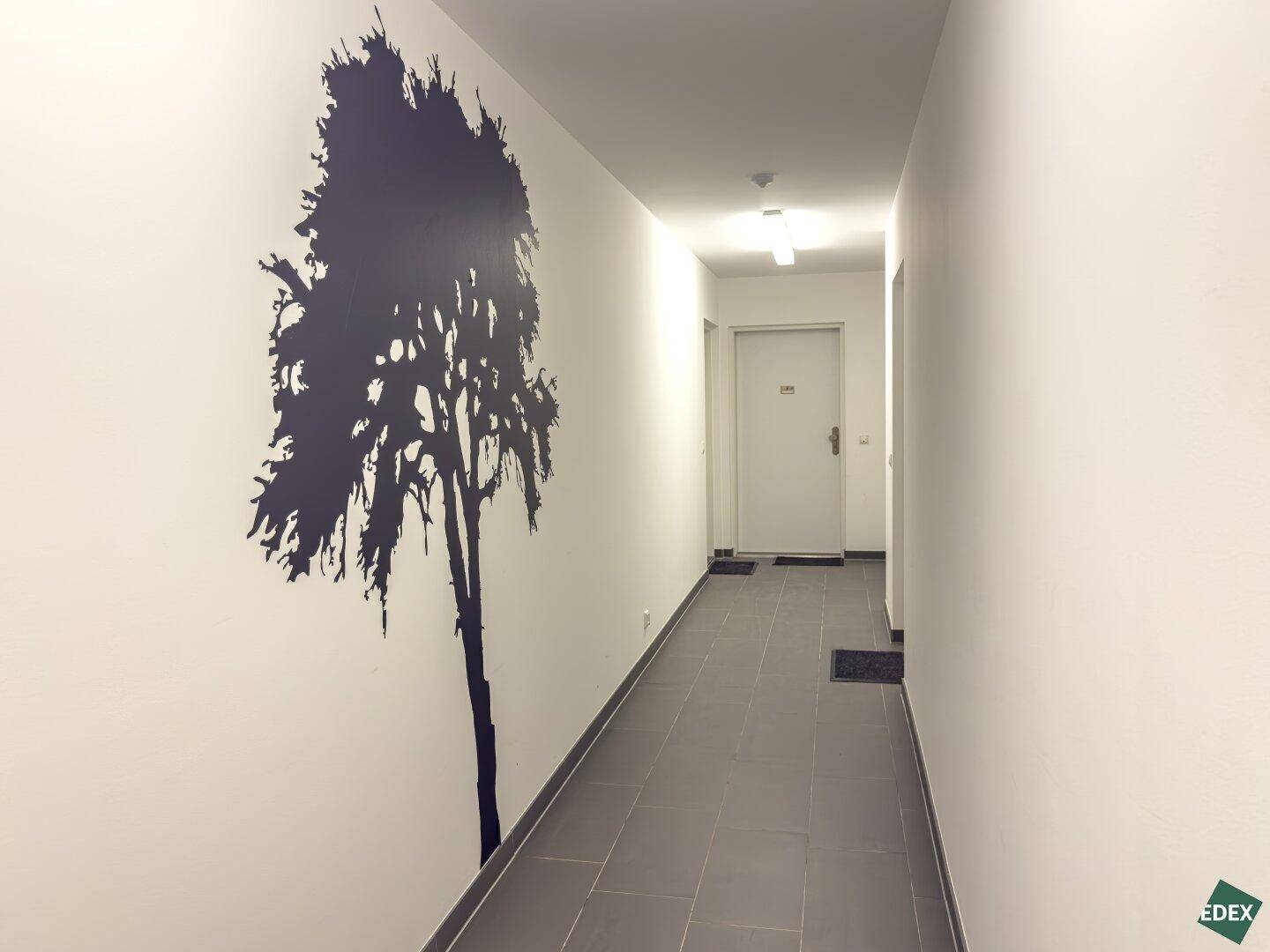 Langer Flur mit Fliesenboden und einem dekorativen Baum-Wandaufkleber, der den Raum belebt.