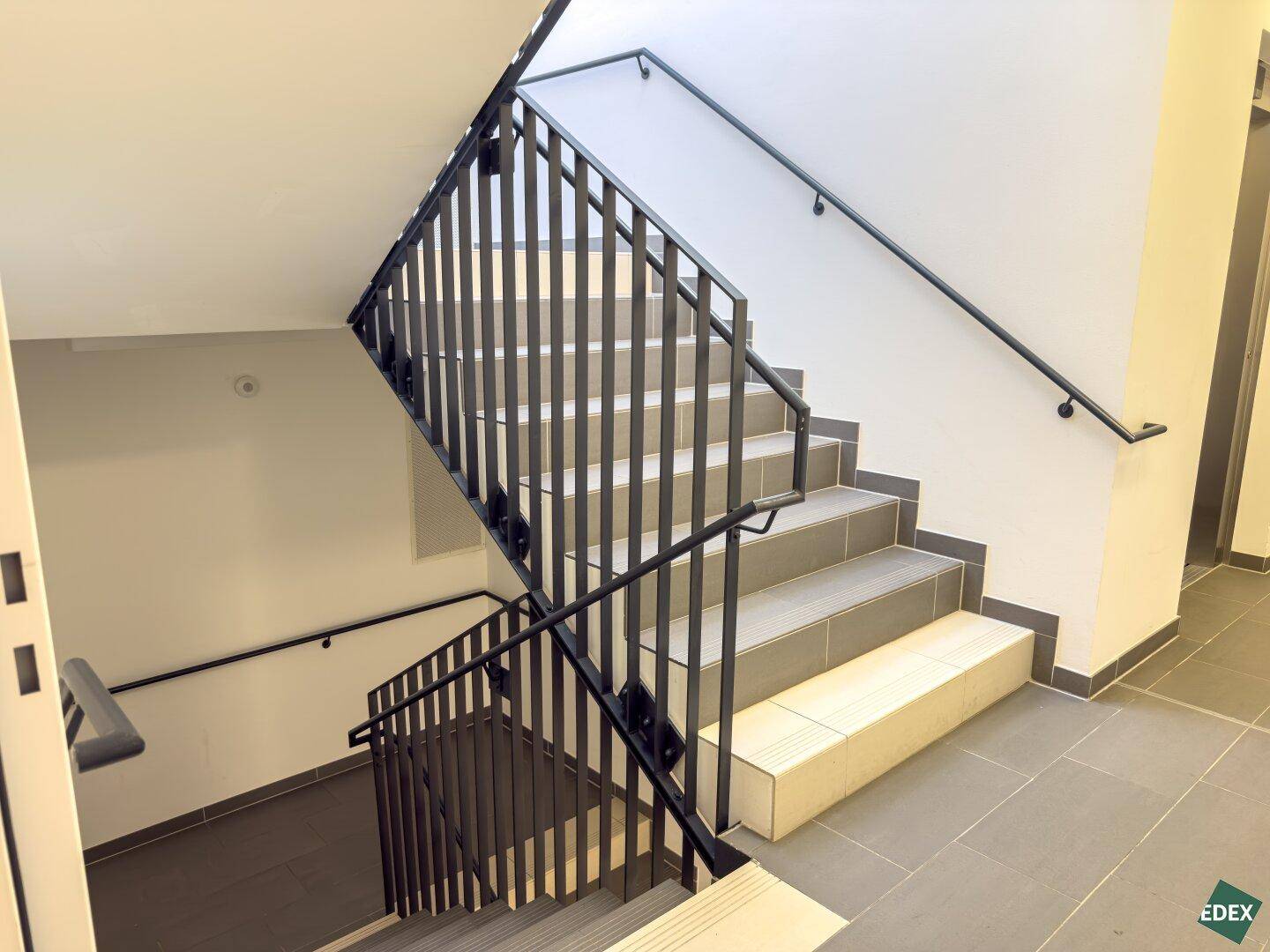 Treppenhaus mit robustem Metallgeländer und Fliesenstufen in einem modernen Gebäude.