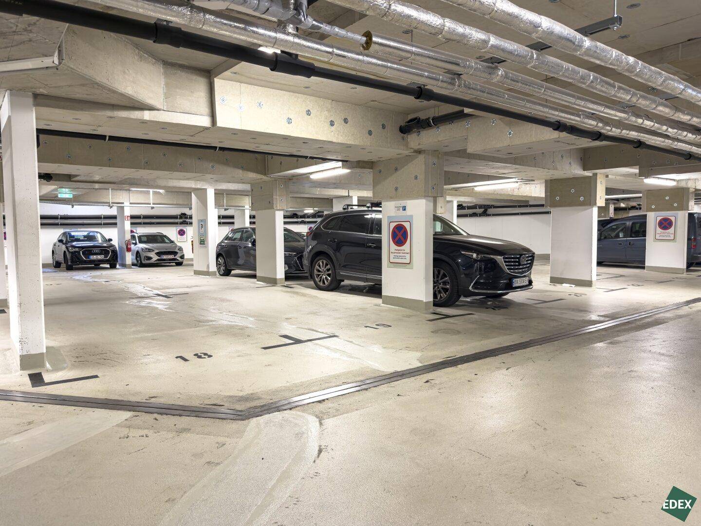 Geräumige Tiefgarage mit mehreren geparkten Autos und Betonstützen.
