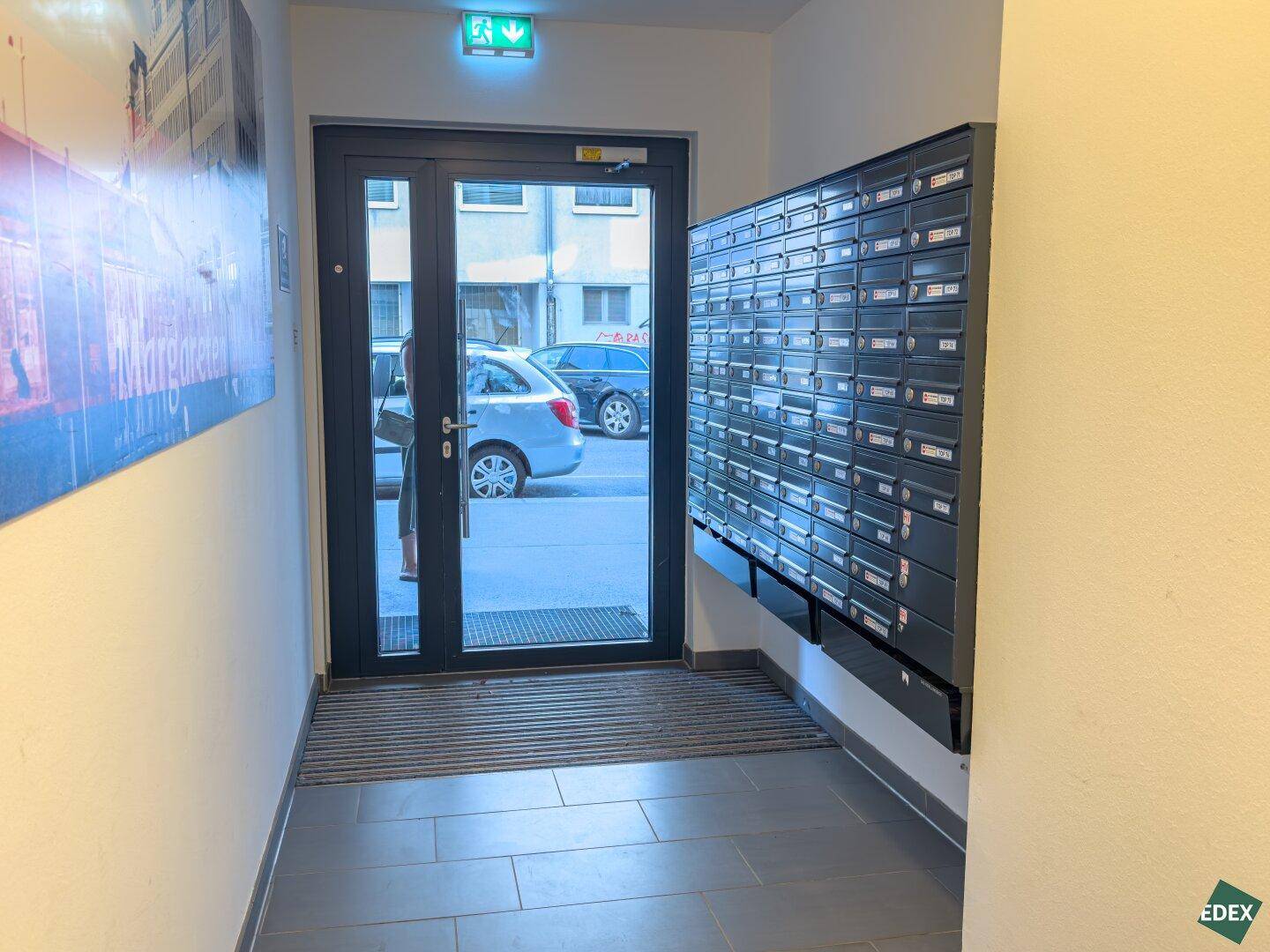 Eingangsbereich des Gebäudes mit Briefkästen und einer Glastür zur Straße.