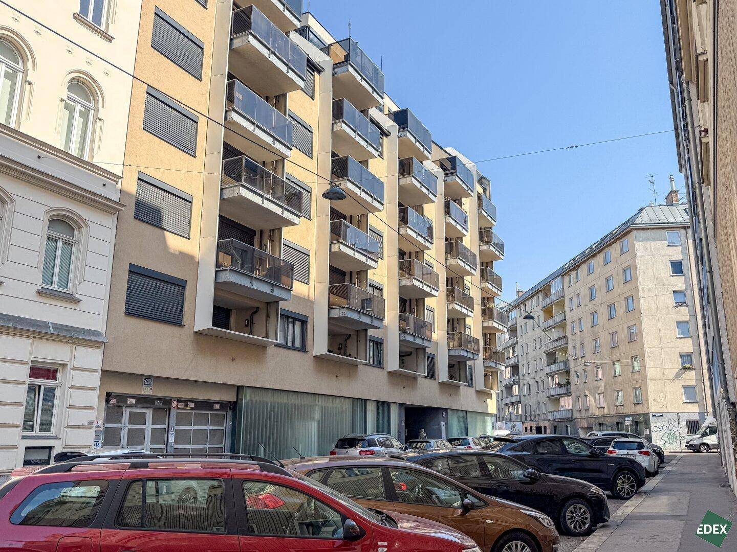 Moderne Wohngebäude mit Balkonen und Jalousien entlang einer belebten Stadtstraße.