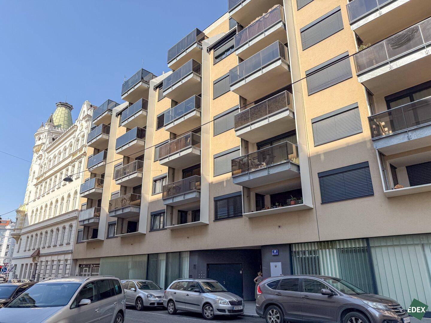 Fassade eines modernen Wohngebäudes mit vielen Balkonen und Fenstern in urbaner Umgebung.