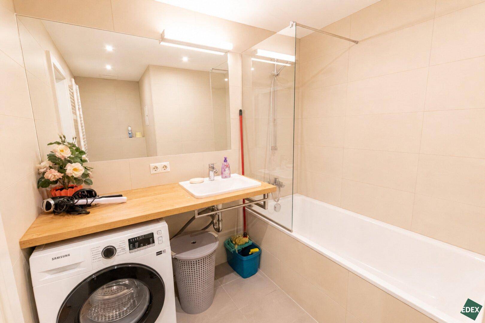 Modernes Badezimmer mit Badewanne, Waschbecken auf Holzplatte und integrierter Waschmaschine.