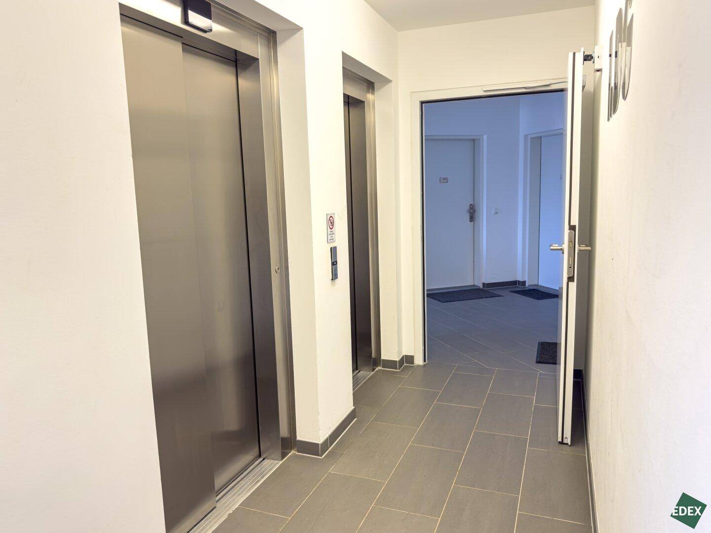 Heller Flur mit zwei Aufzügen und Zugang zu den Wohnungen in einem Mehrfamilienhaus.