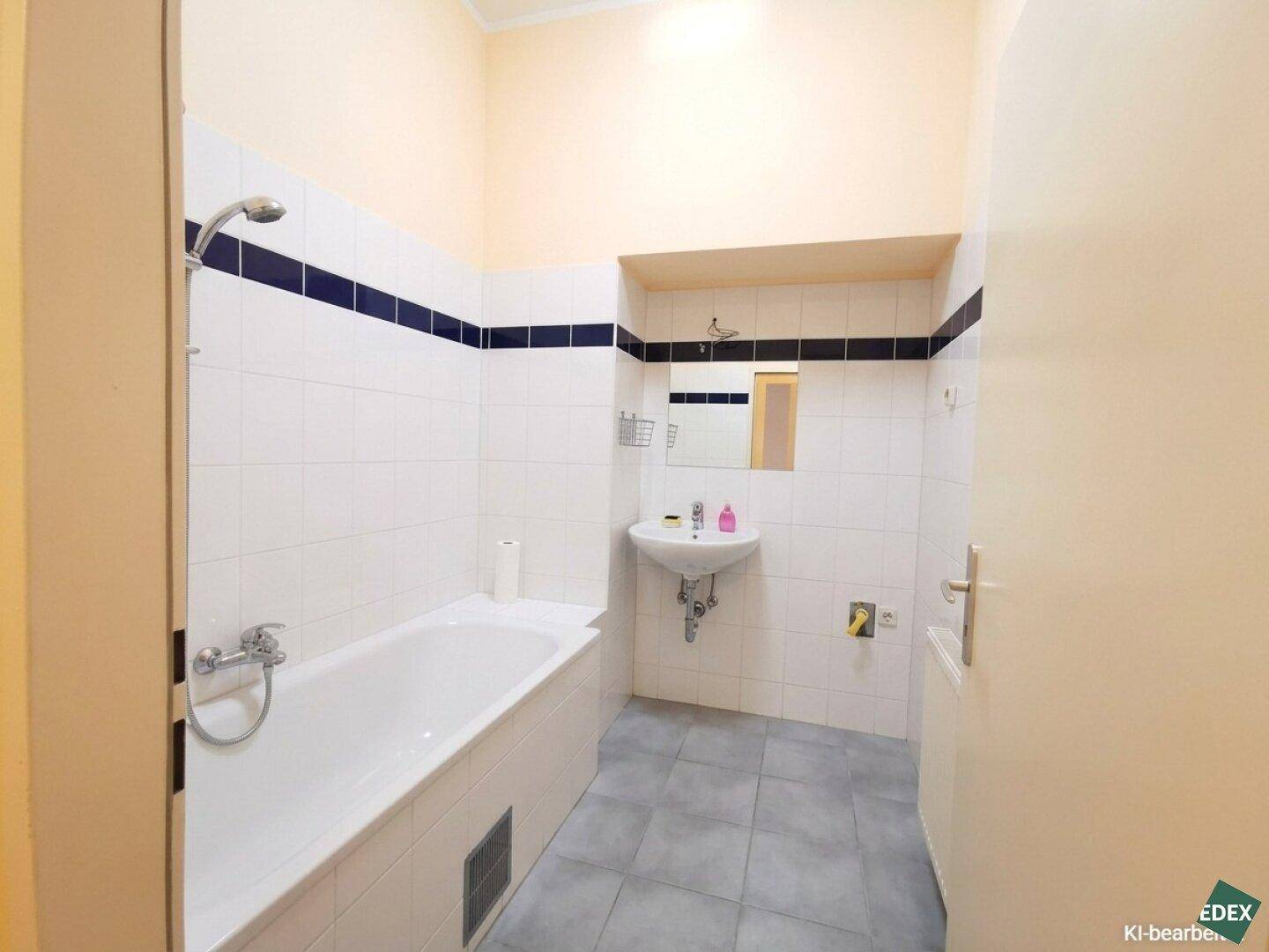 Badezimmer mit Badewanne, Waschbecken und weißen Fliesen, verziert mit einem dunklen Akzentstreifen.