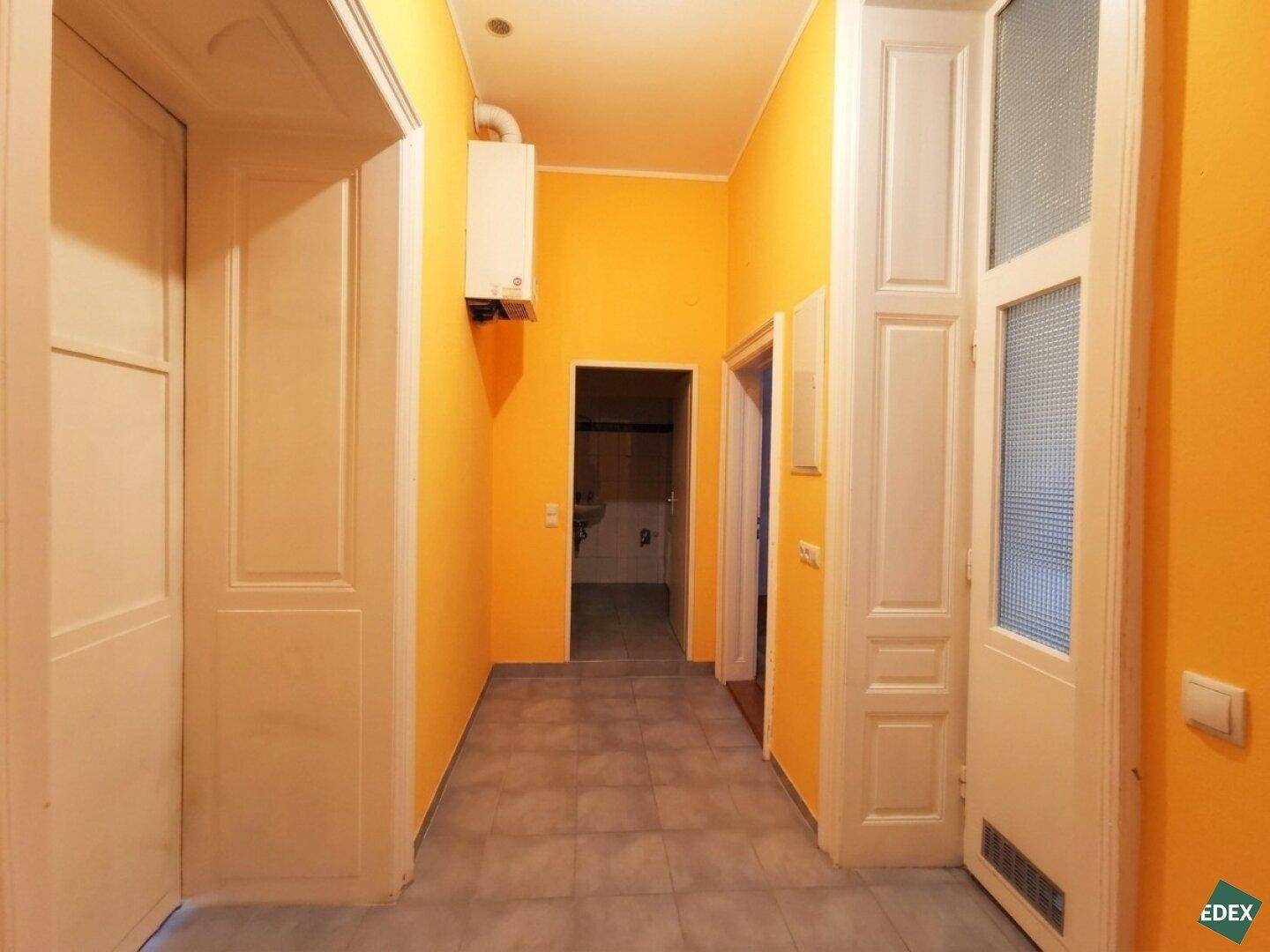Heller Flur mit leuchtend orangefarbenen Wänden, Fliesenboden und mehreren Türen, inklusive Warmwasserbereiter.
