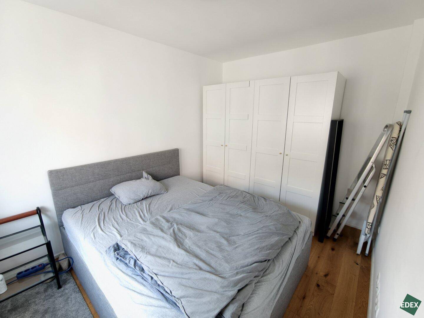 Schlafzimmer mit Holzboden, Bett und einem weißen Kleiderschrank an der Wand.