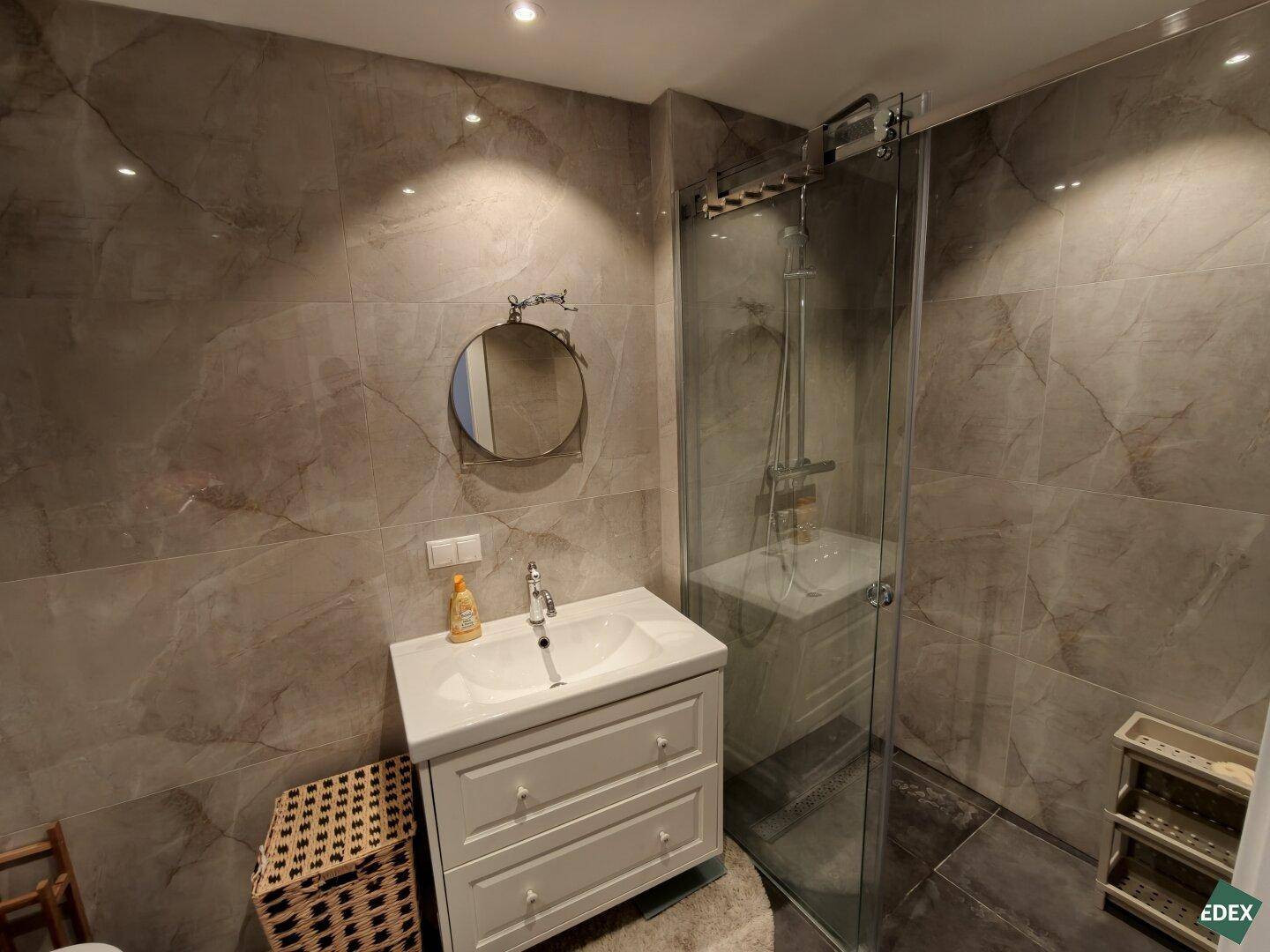 Helles Badezimmer mit zeitgemäßen grauen Fliesen, Duschkabine und Waschtisch.