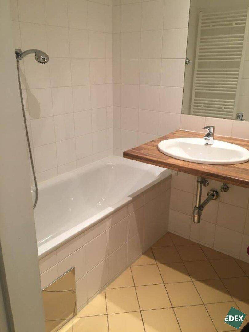 Badezimmer mit Badewanne, Einzelwaschbecken auf Holzplatte und weißen Fliesen an Wänden und Boden.