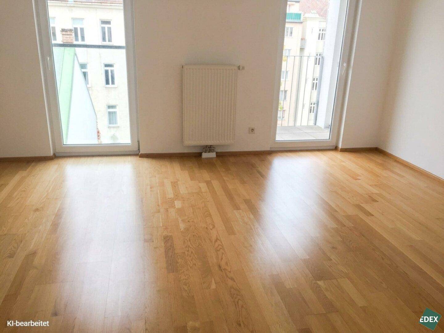 Leeres Zimmer mit hellem Parkettboden und zwei großen Fenstern, die viel Tageslicht hereinlassen.