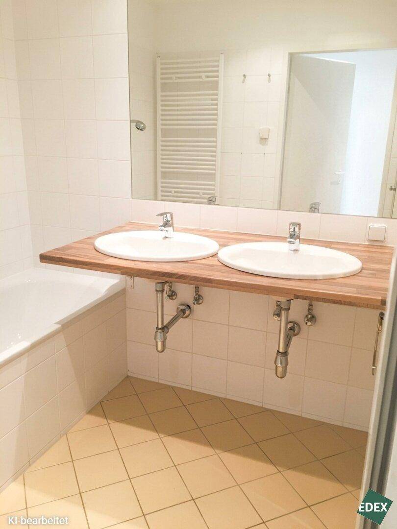 Modernes Badezimmer mit Doppelwaschbecken auf Holzplatte, Badewanne und hellen Fliesen.