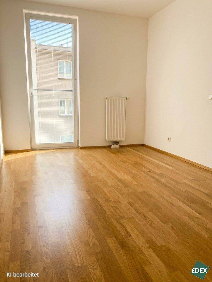 Helles, leeres Zimmer mit Parkettboden und großem Fenster, das viel natürliches Licht bietet.