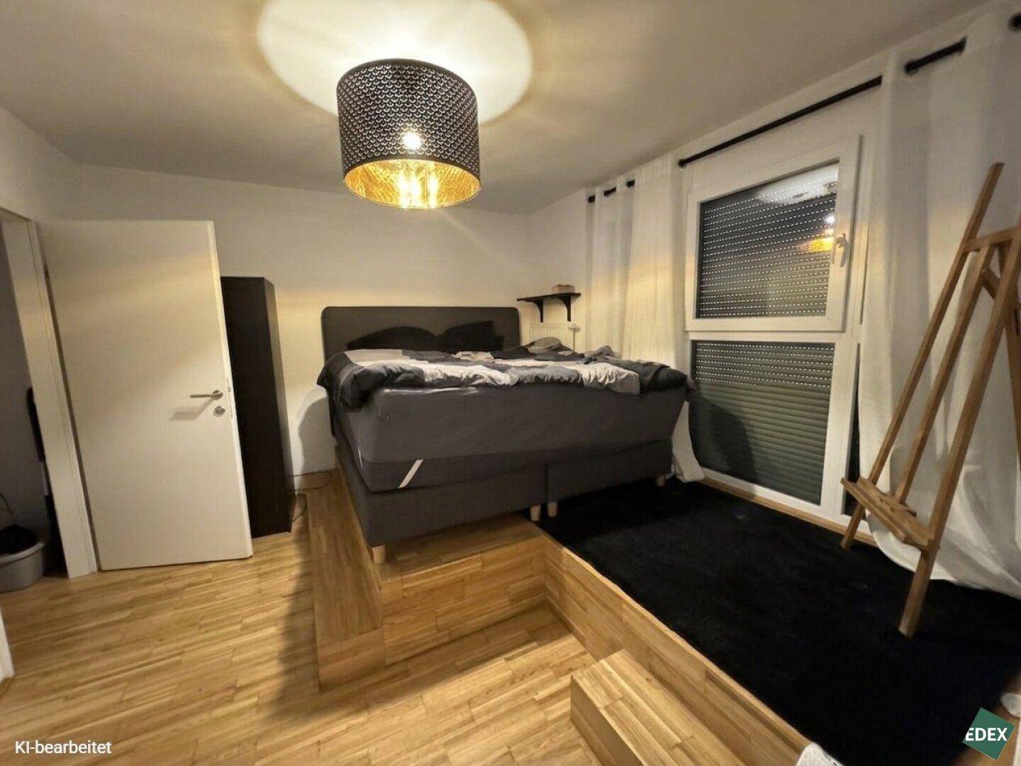 Schlafzimmer mit erhöhtem Bettbereich, Holzfußboden und großem Fenster.