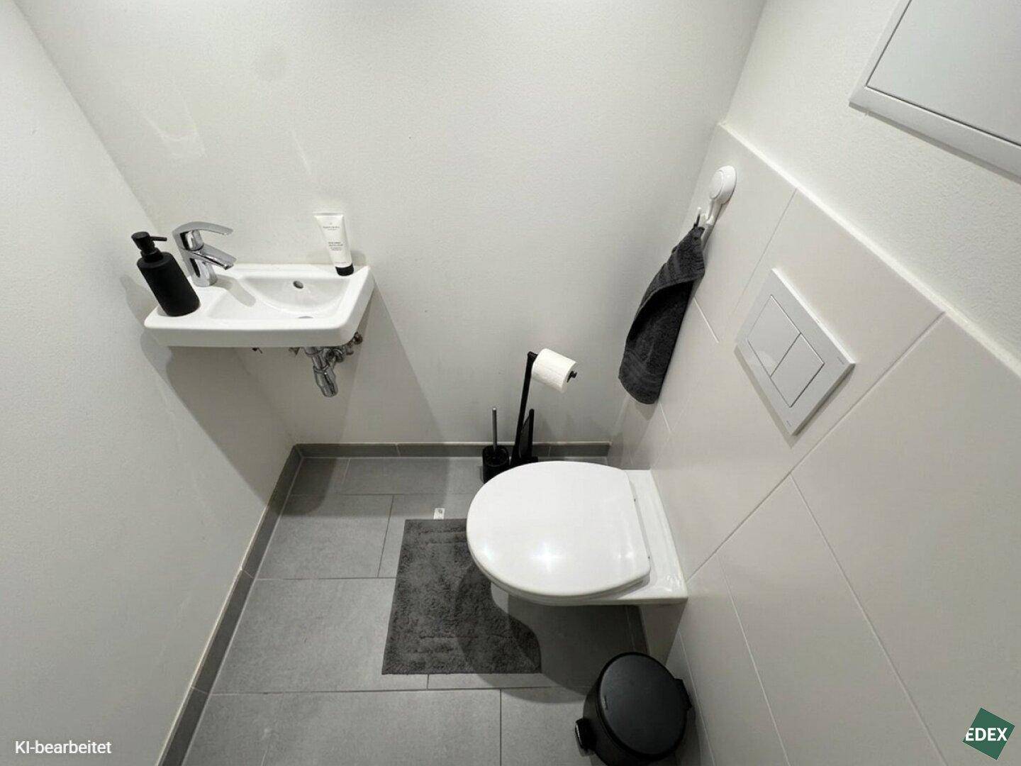 Kleines Gäste-WC mit wandhängendem WC, Waschbecken und modernen Fliesen.
