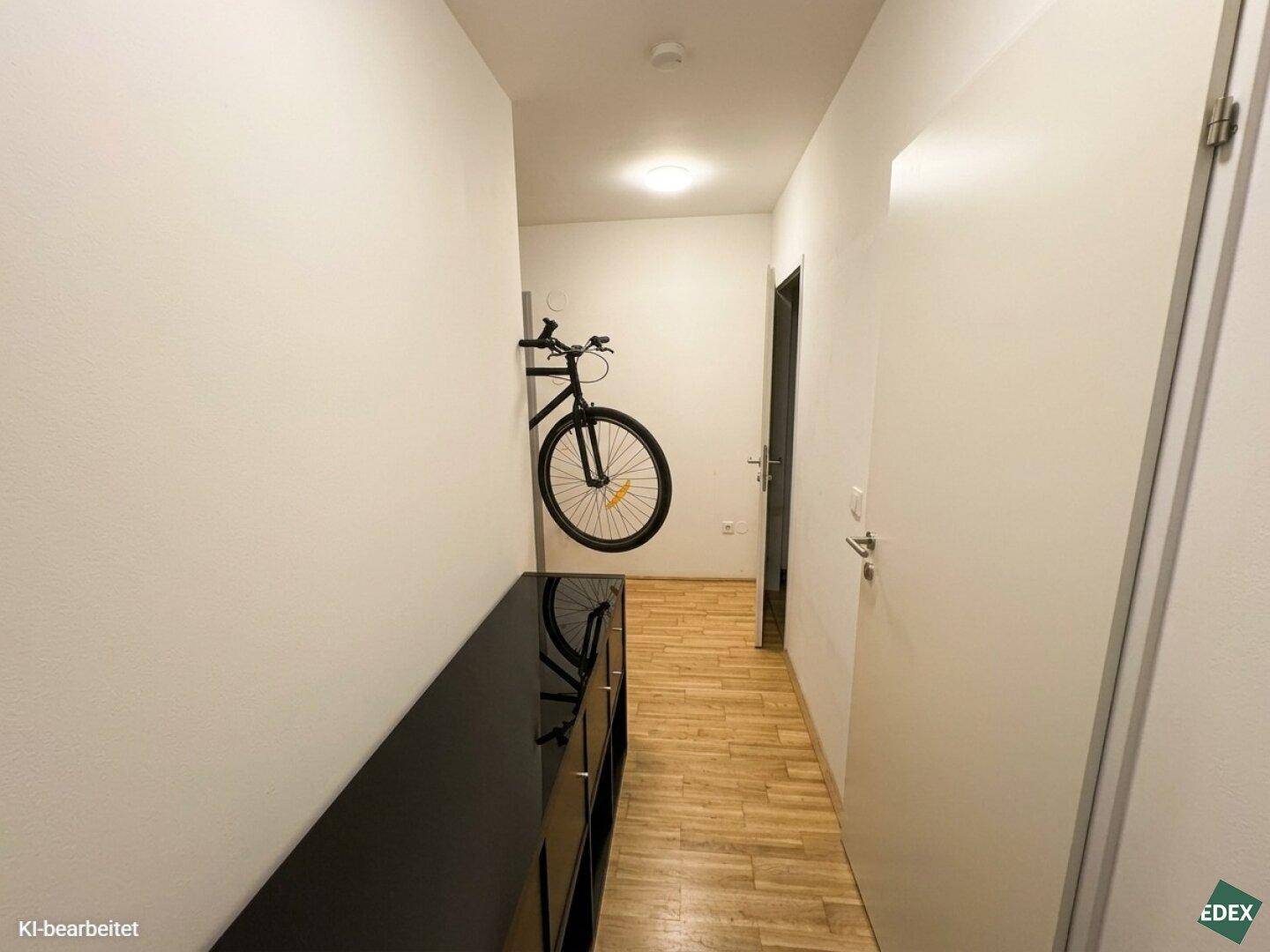 Heller Flur mit Holzfußboden, einer Kommode und Fahrradaufhängung an der Wand.