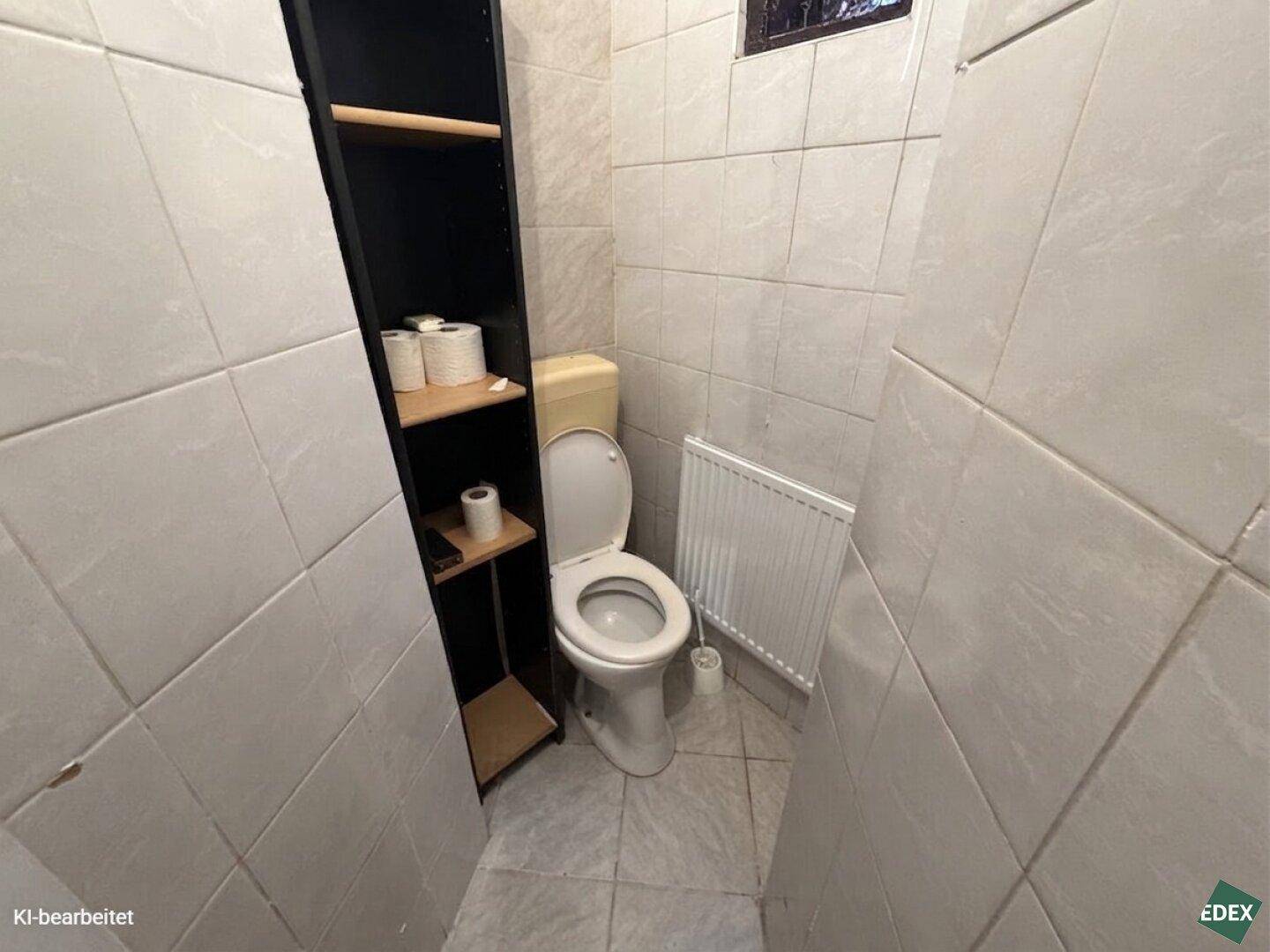 Kleines separates WC mit Toilette, schmalem Regal und gefliesten Wänden.
