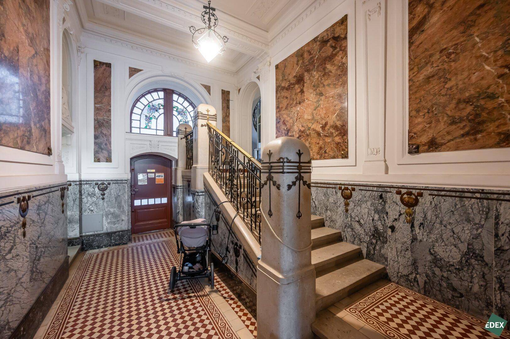 Prunkvoller Eingangsbereich eines Altbaus mit Marmorverkleidung, kunstvoller Treppe und gemusterten Bodenfliesen.