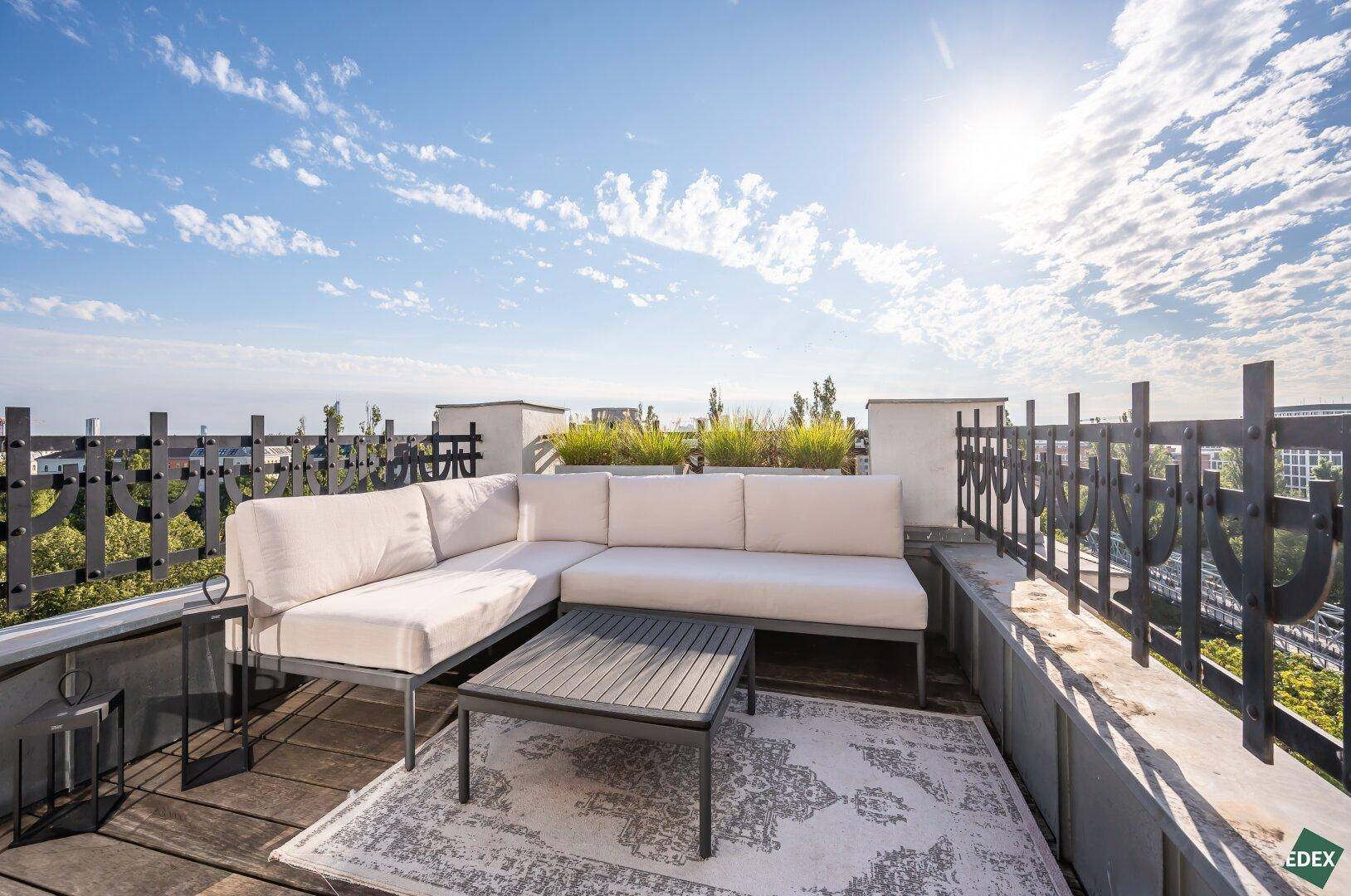Geräumige Dachterrasse mit bequemen Loungemöbeln unter blauem Himmel.