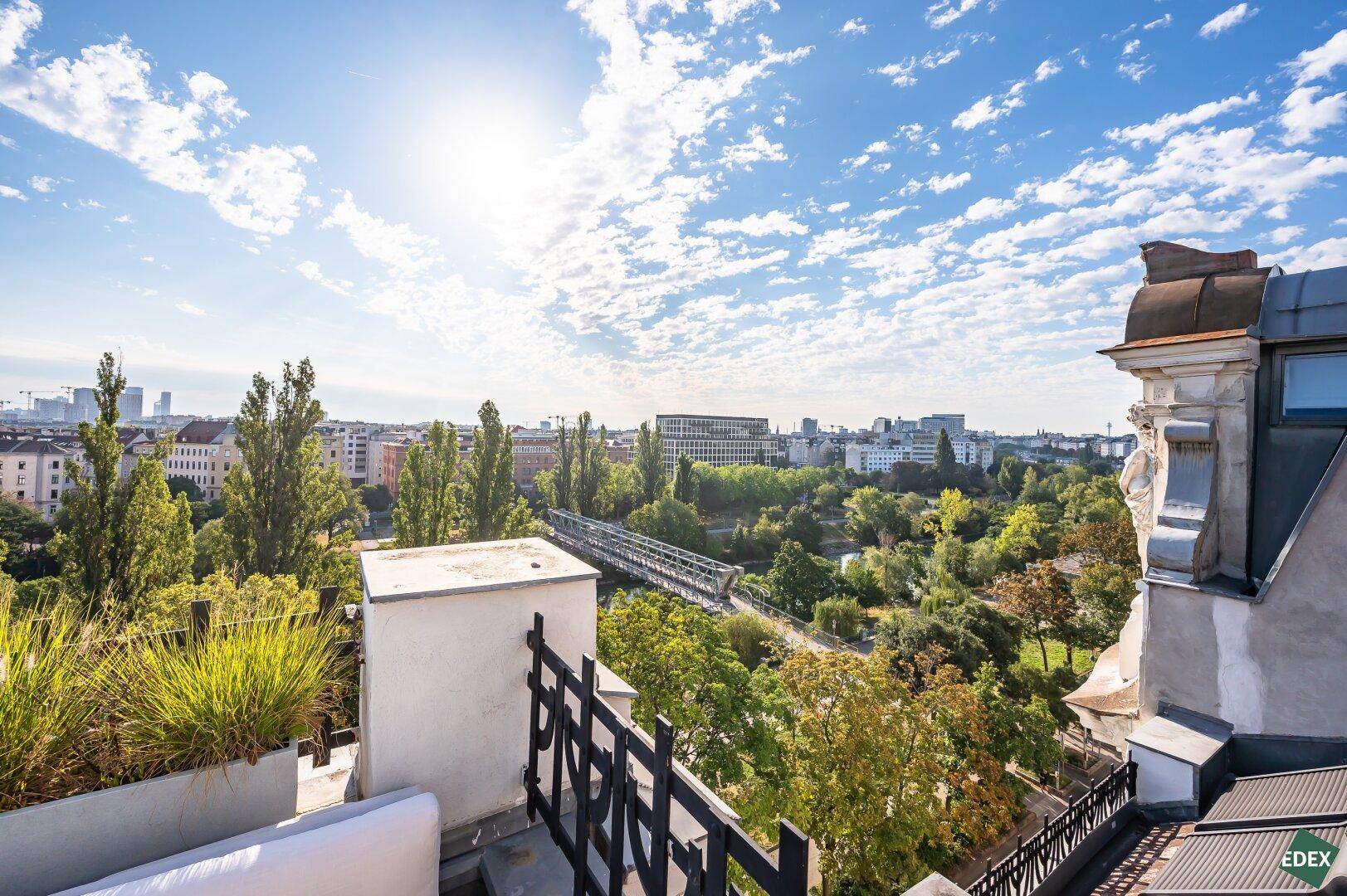 Weitläufiger Panoramablick von der Dachterrasse über einen grünen Park und die Stadtlandschaft bei Sonnenschein.