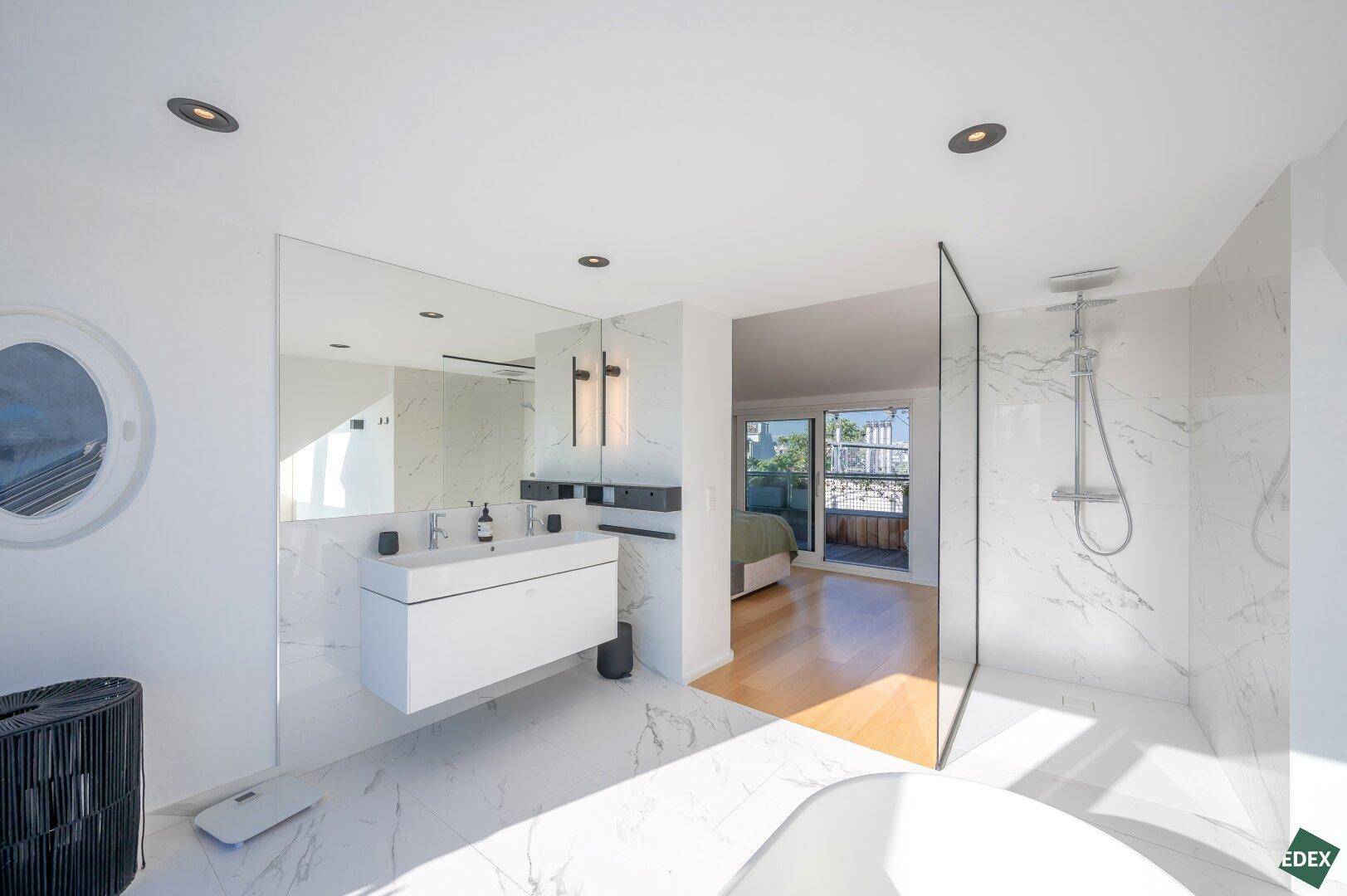 Elegantes Badezimmer mit begehbarer Dusche, Doppelwaschbecken und Marmorfliesen, offen zum Schlafzimmer.