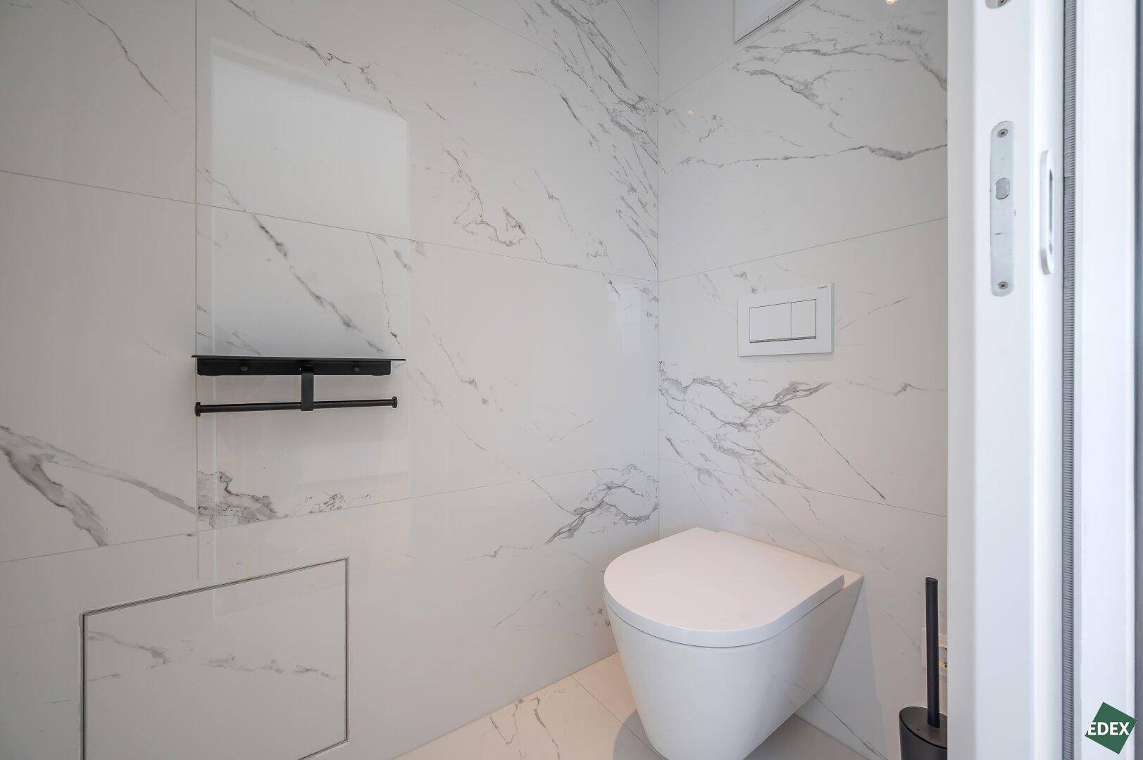 Modernes Gäste-WC mit wandhängender Toilette und eleganten Marmorfliesen in minimalistischem Design.