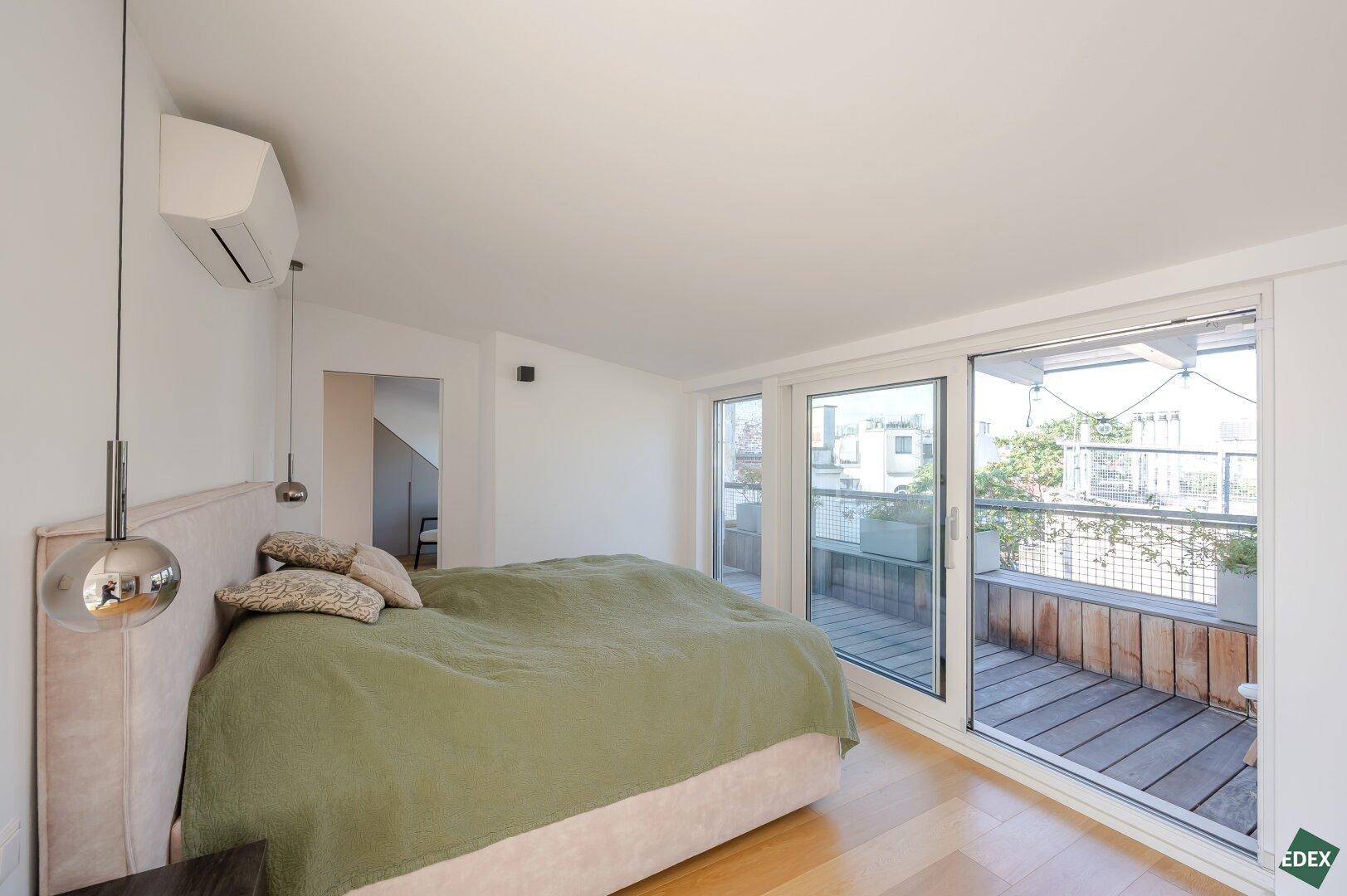 Geräumiges Schlafzimmer mit Holzboden und großen Fenstern zur Terrasse.
