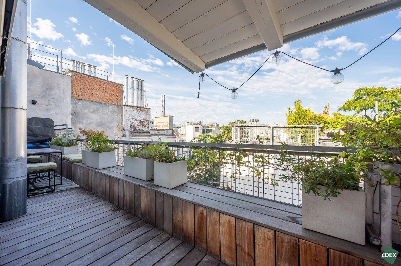 Geräumige Dachterrasse mit Holzbelag, Pflanzen und gemütlicher Beleuchtung, ideal für entspannte Abende.