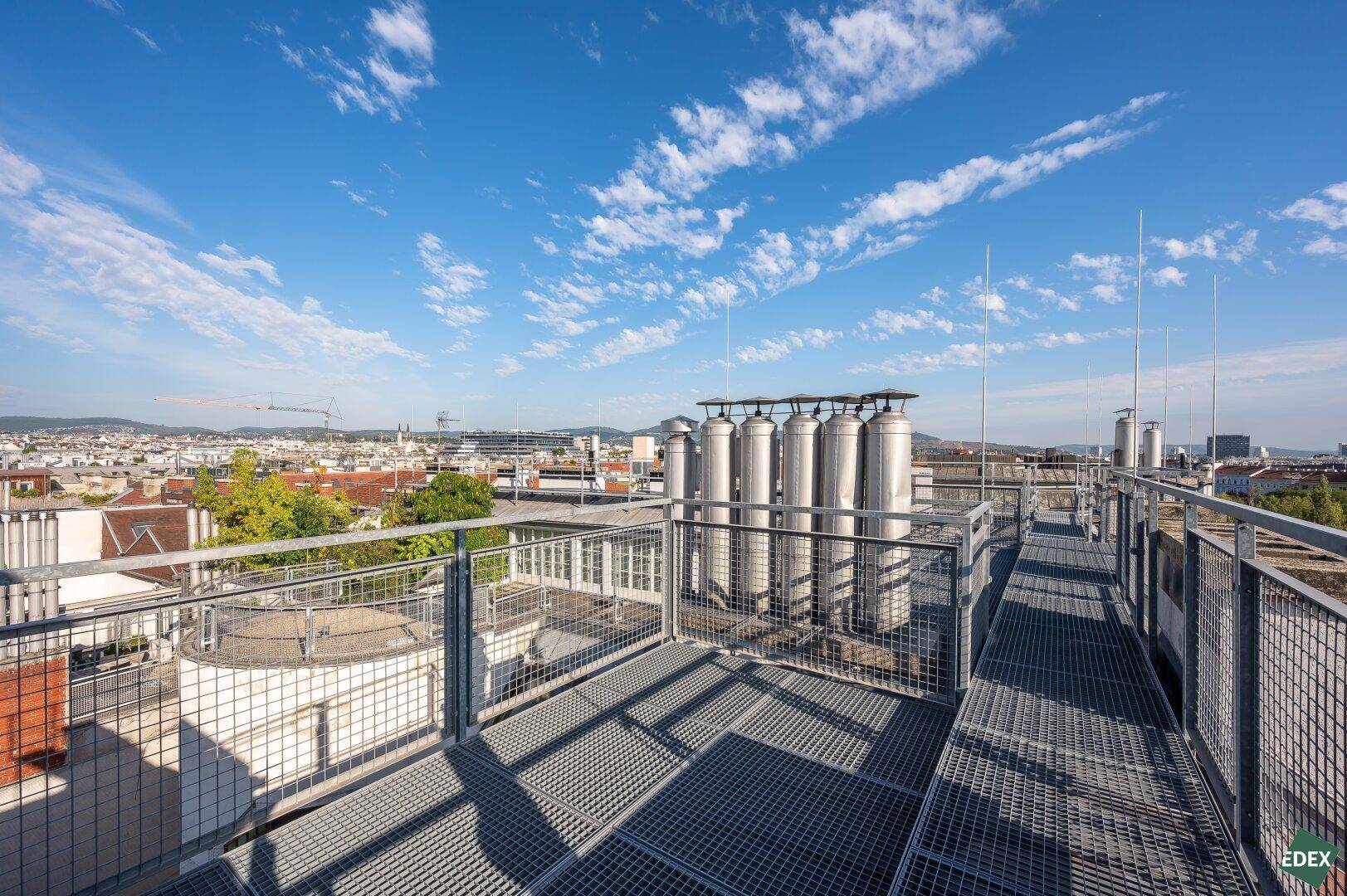 Weitläufige Dachfläche mit technischen Anlagen und Gitterrosten, bietet einen weiten Blick über die Stadtlandschaft.
