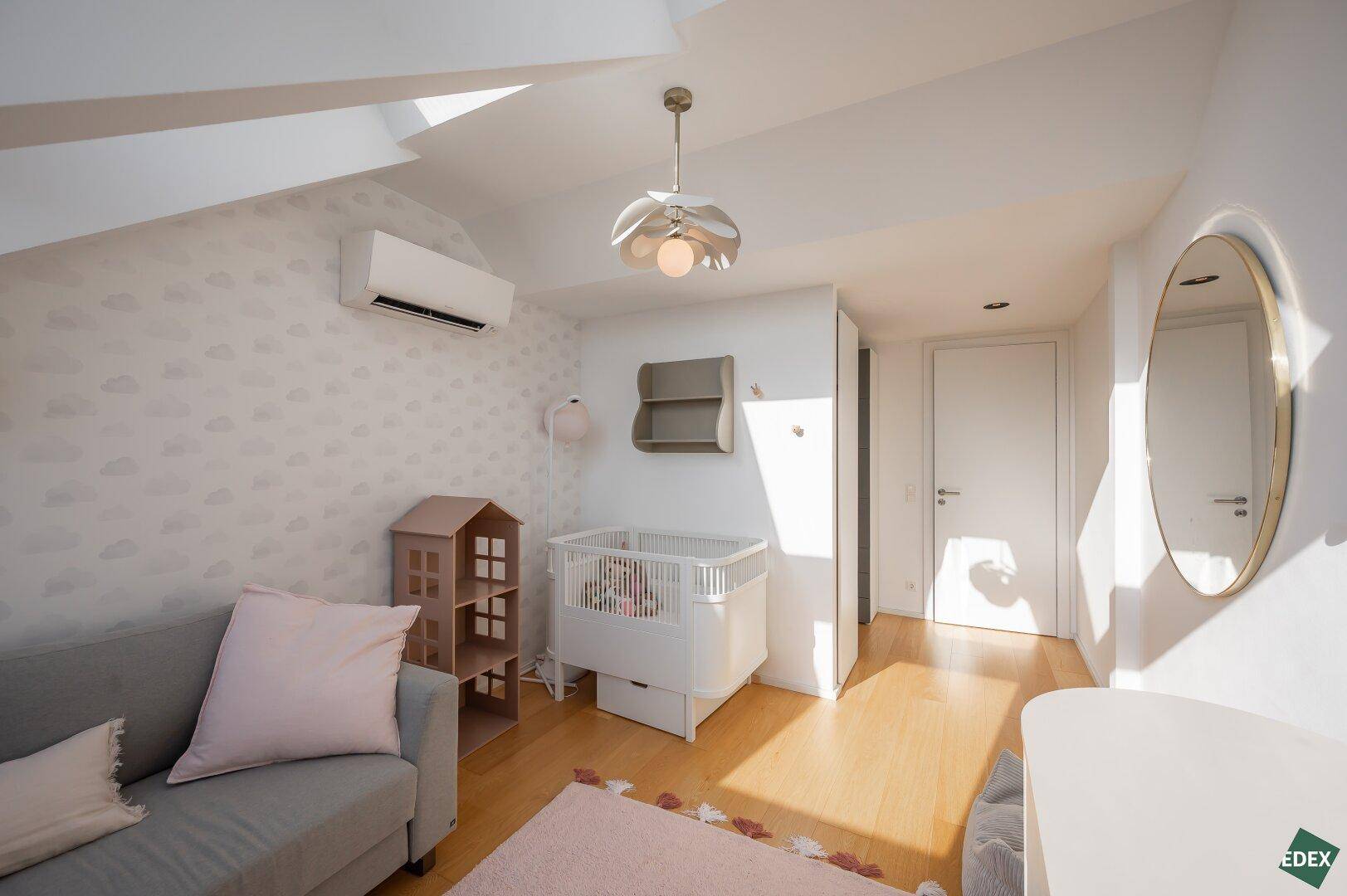 Helles Kinderzimmer mit Dachschrägen, Babybett und gemütlichem Sofa.