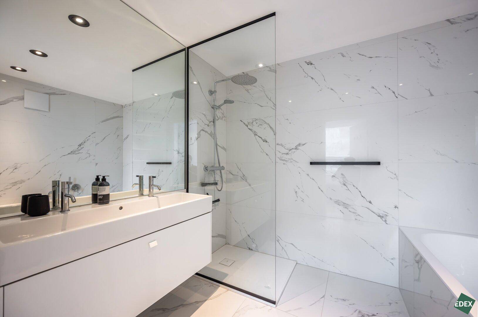 Elegantes Badezimmer mit großer begehbarer Dusche, Einzelwaschbecken und luxuriösen Marmorfliesen.