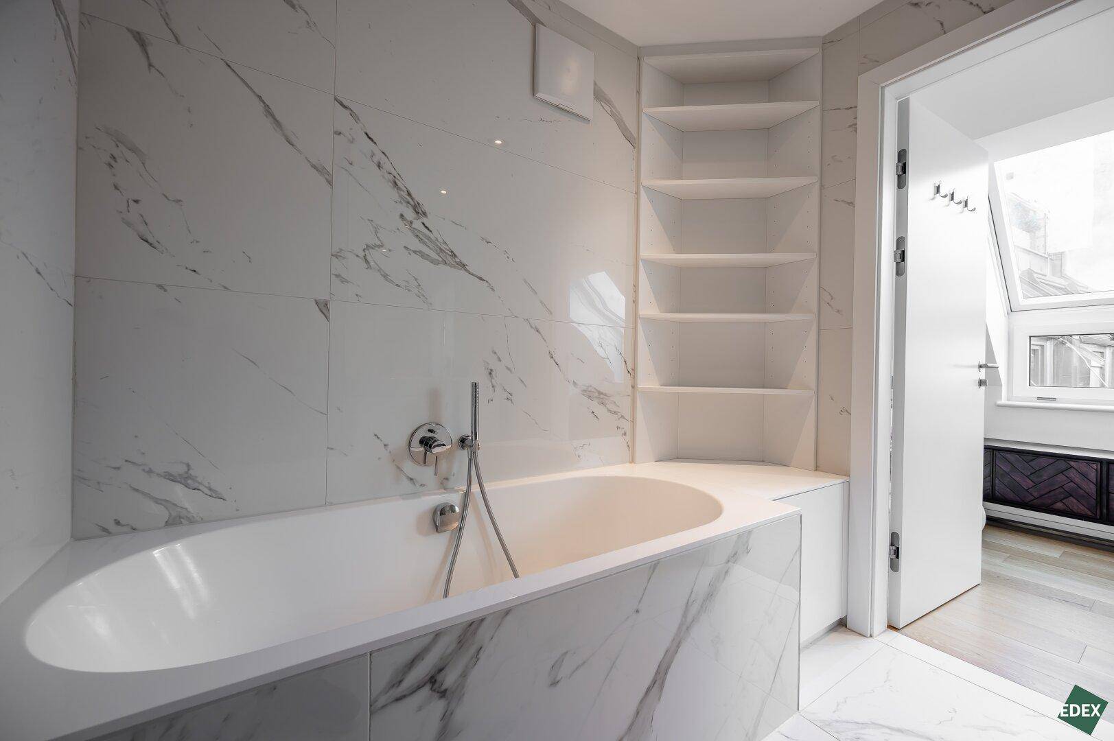 Helles Badezimmer mit eingebauter Badewanne, Marmorfliesen und praktischen Wandregalen für Stauraum.