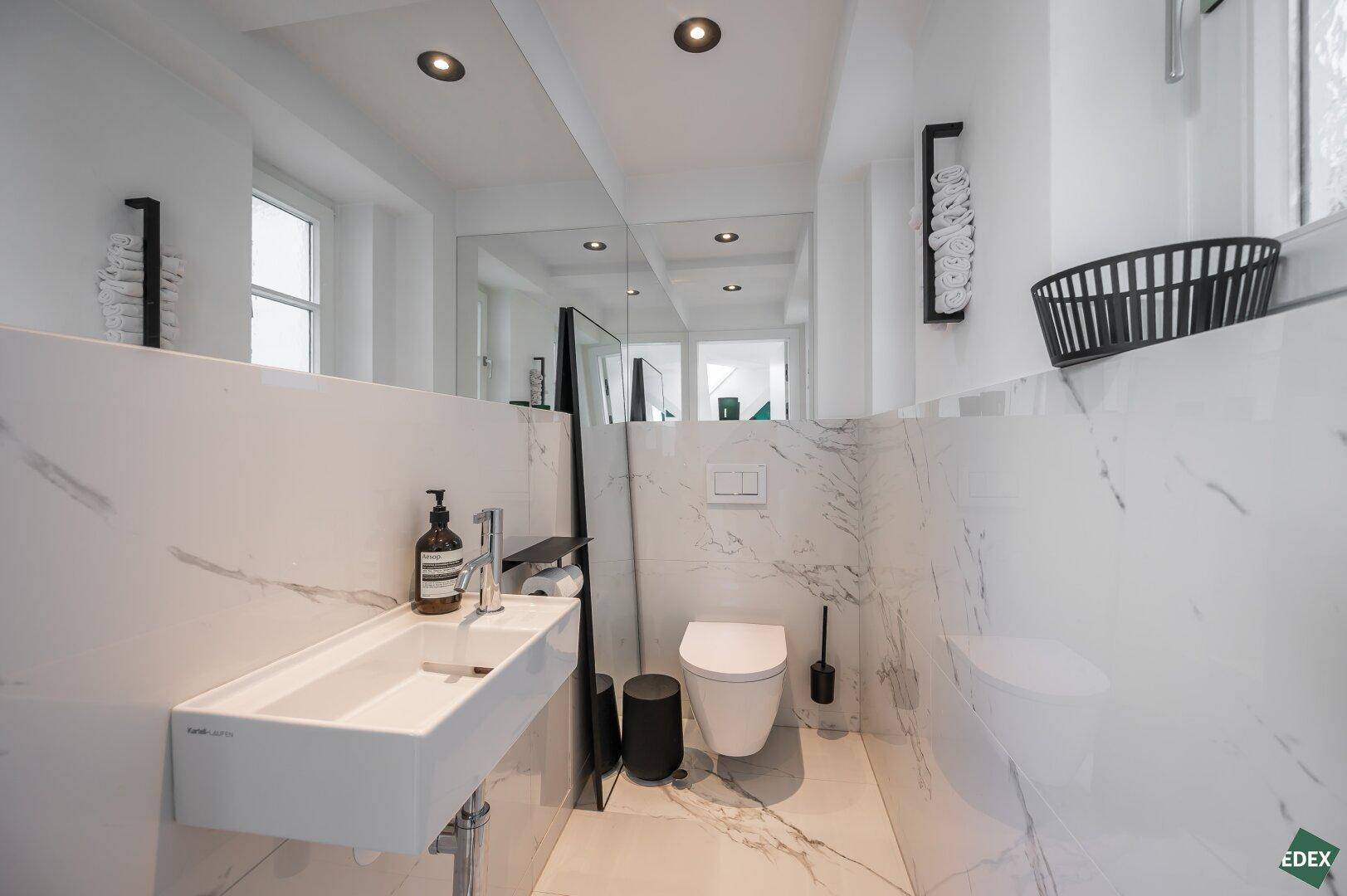 Stilvolles Gäste-WC mit modernem Waschbecken, wandhängender Toilette und großem Spiegel, alles in Marmoroptik.
