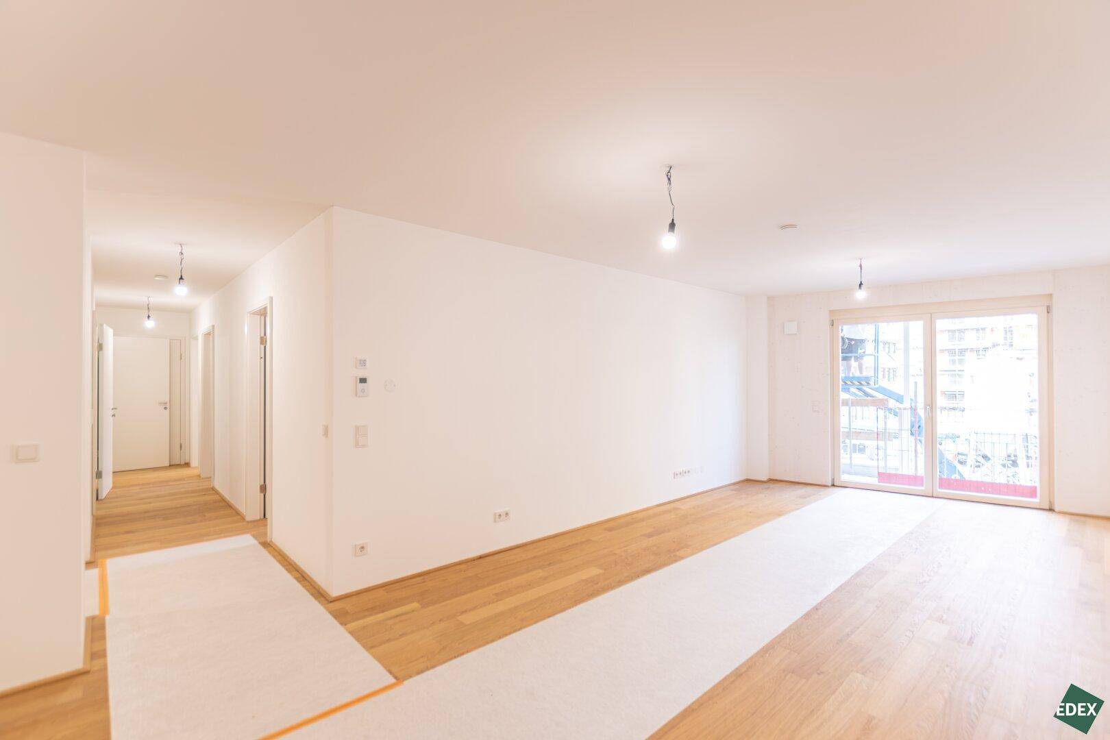 Geräumiges, helles Wohnzimmer mit Holzboden und Zugang zu einem Balkon, bereit für den Einzug.