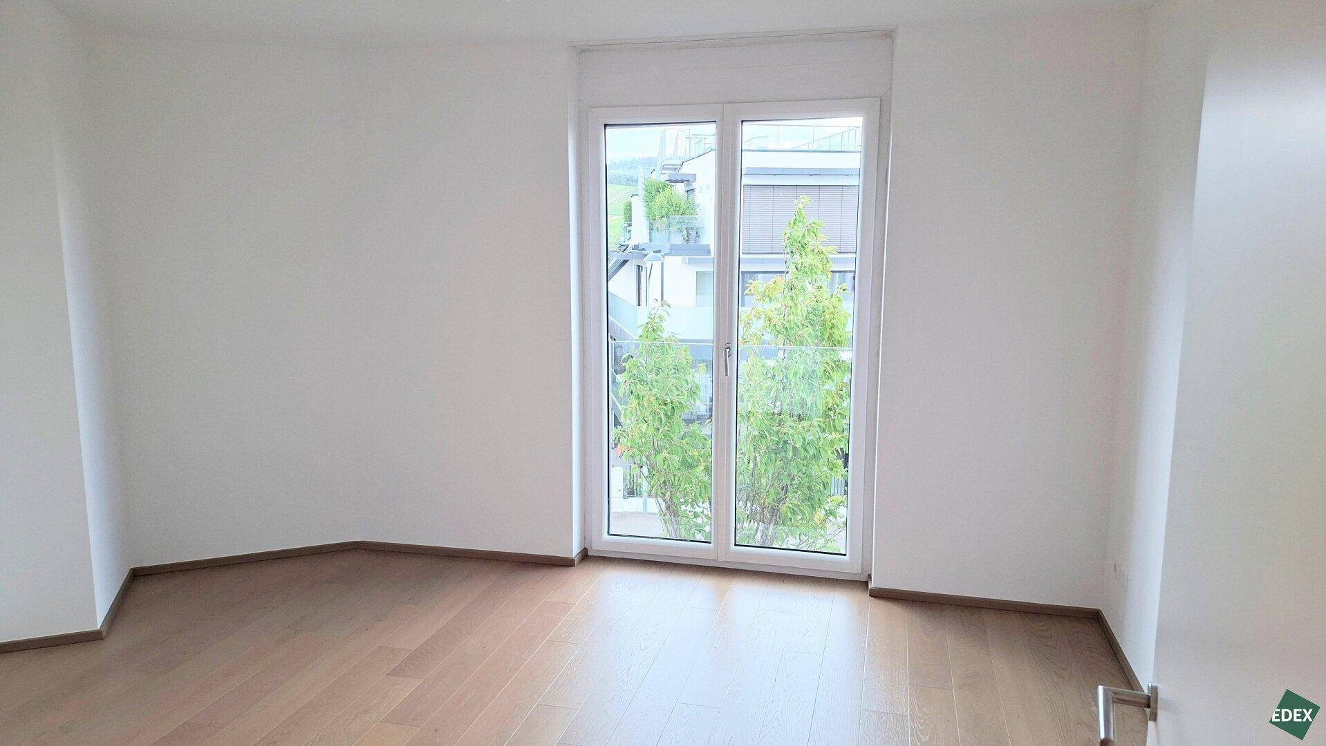 Geräumiges Zimmer mit Holzboden und großem Fenster, das viel Tageslicht hereinlässt.