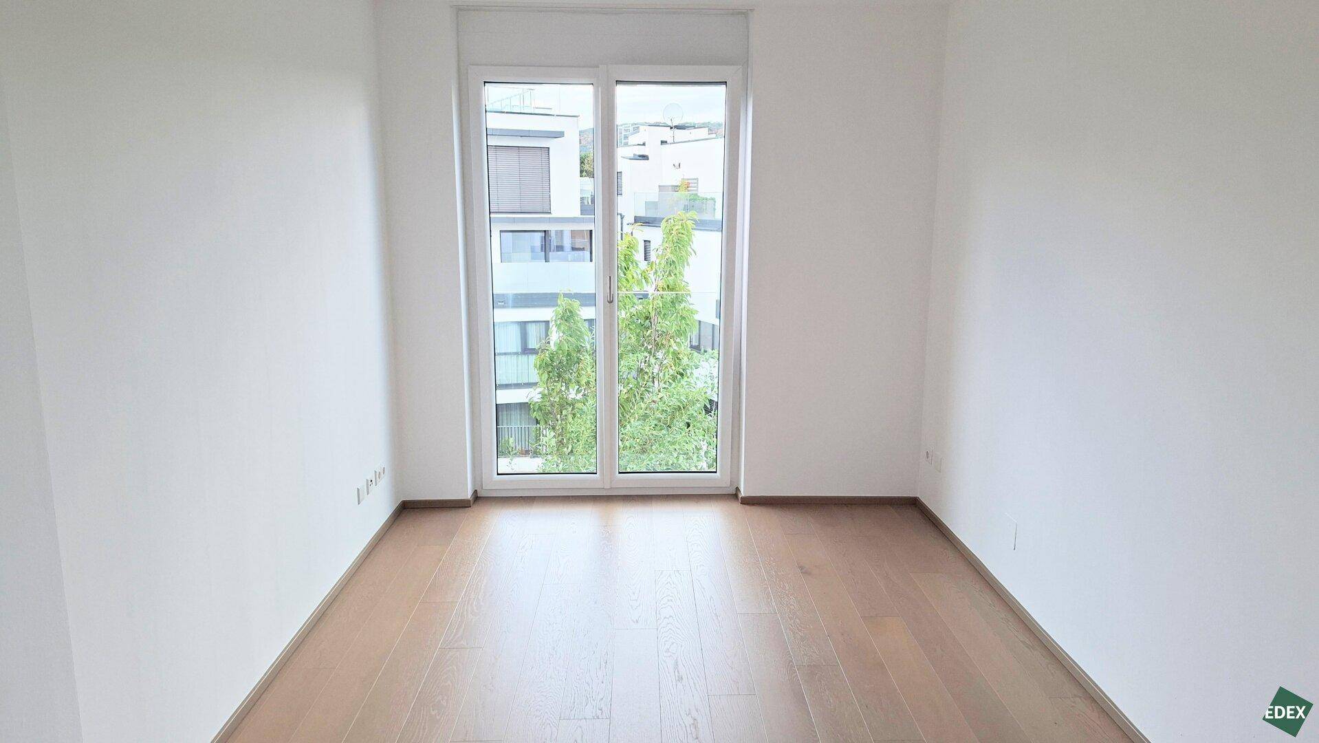 Helles Schlafzimmer mit Holzboden und großem Fenster mit Blick ins Grüne.