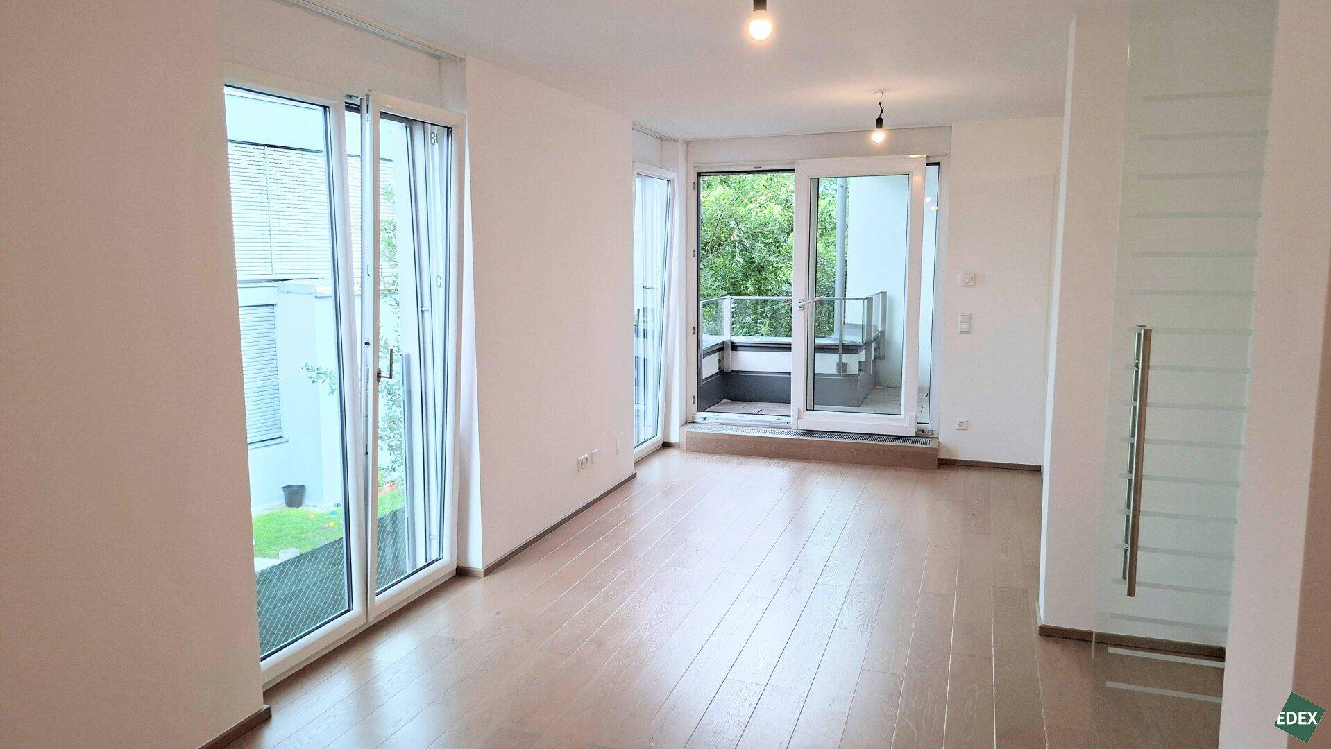 Geräumiges, helles Wohnzimmer mit Holzboden und mehreren Fenstern sowie Balkonzugang.