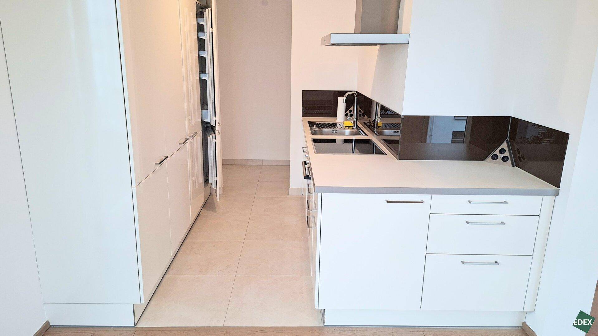 Moderne Einbauküche in Weiß mit integrierten Geräten, Spüle und Dunstabzugshaube.