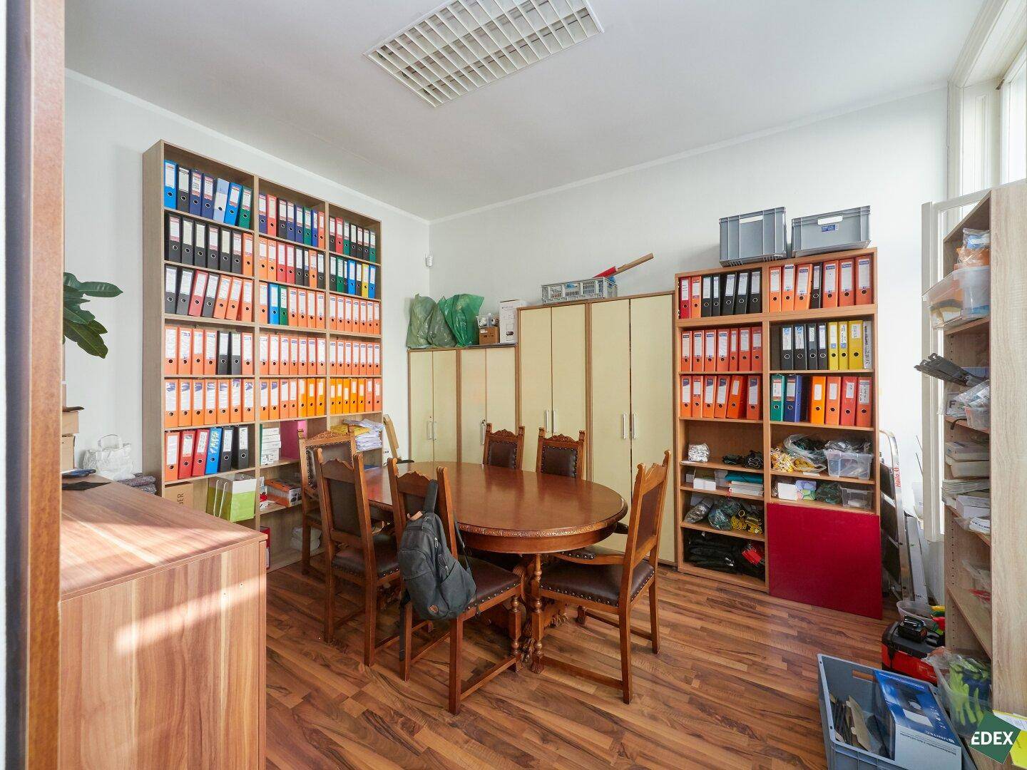 Besprechungsraum mit großem ovalen Tisch, Stühlen und umfangreichen Regalen voller Aktenordner.