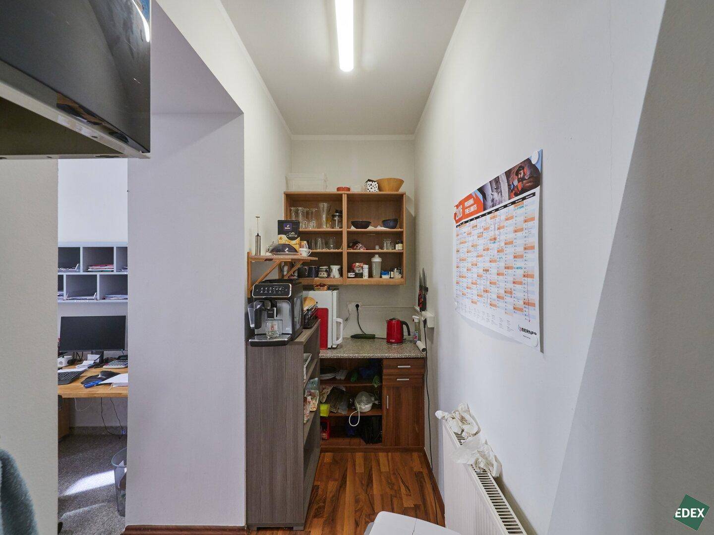 Kleine Küchenzeile oder Pausenraum mit Kaffeemaschine, Regalen und einer Arbeitsplatte.